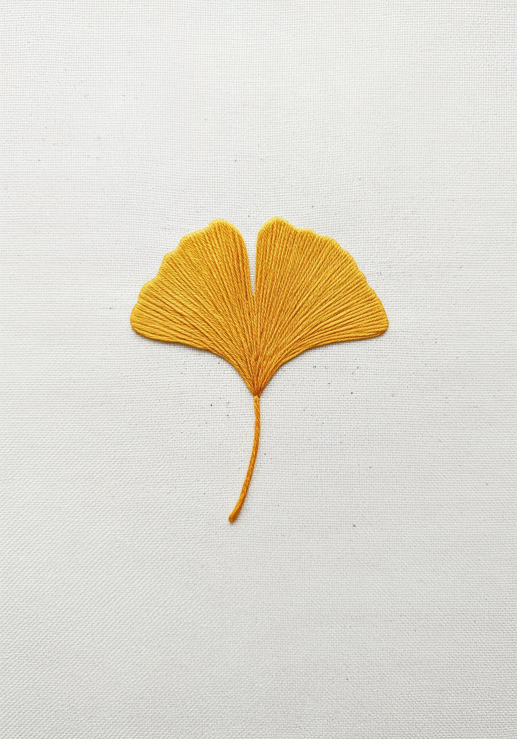 A single ginkgo leaf embroidered in golden yellow thread with angled satin stitches.