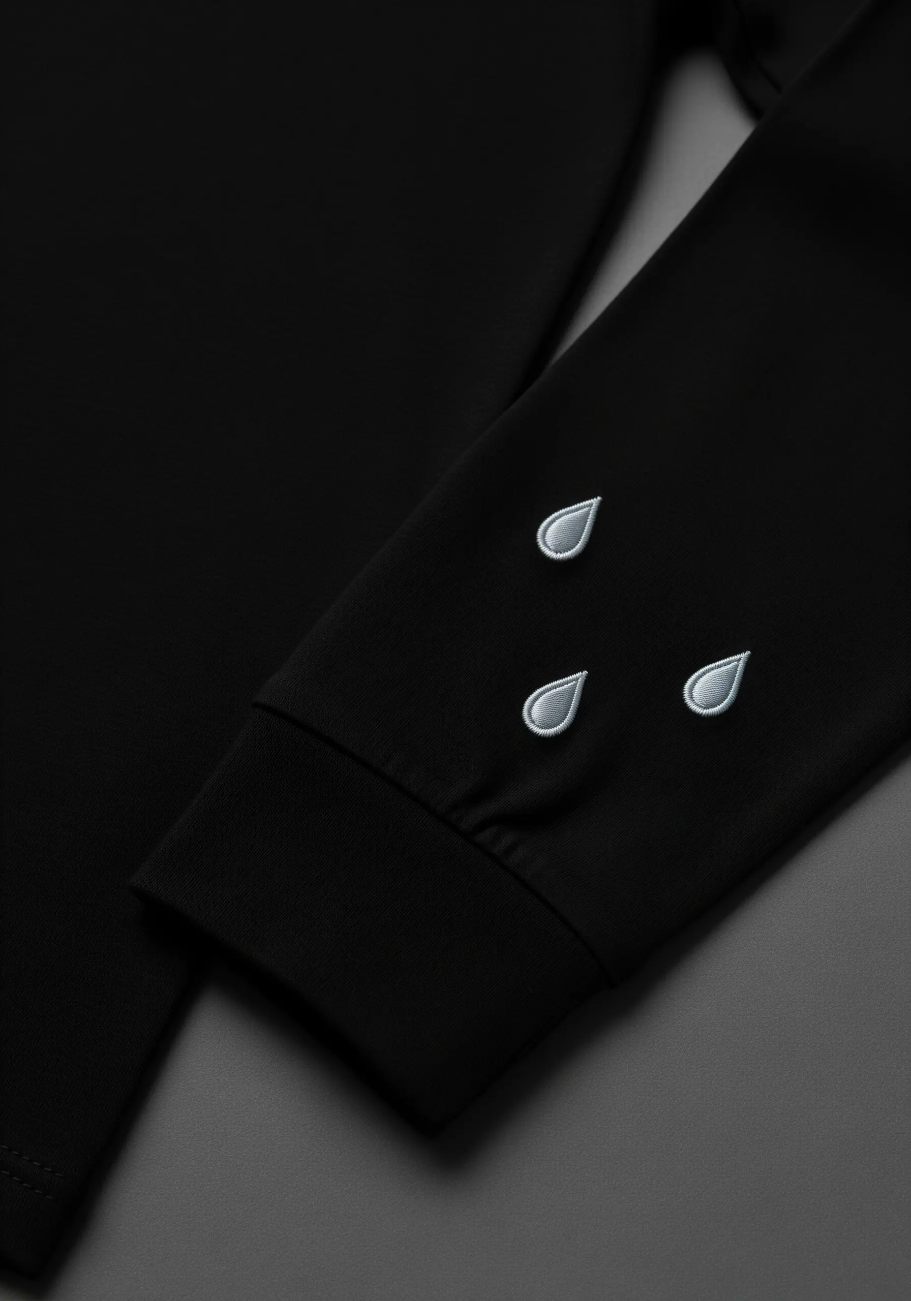 Three embroidered raindrops with light blue fill and dark outlines on a black sleeve.