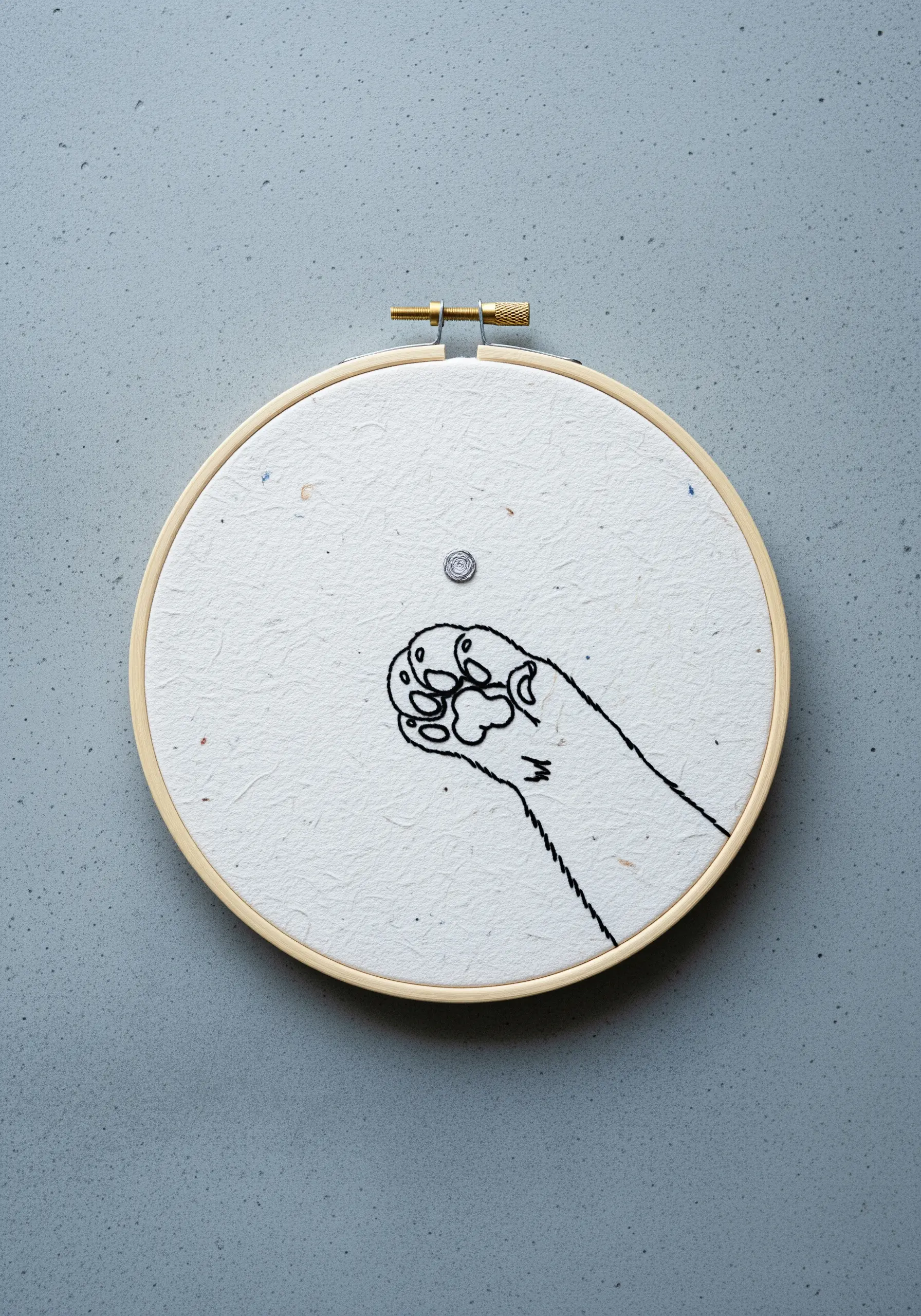 Line art embroidery of a cat's paw stitched directly onto handmade textured paper.