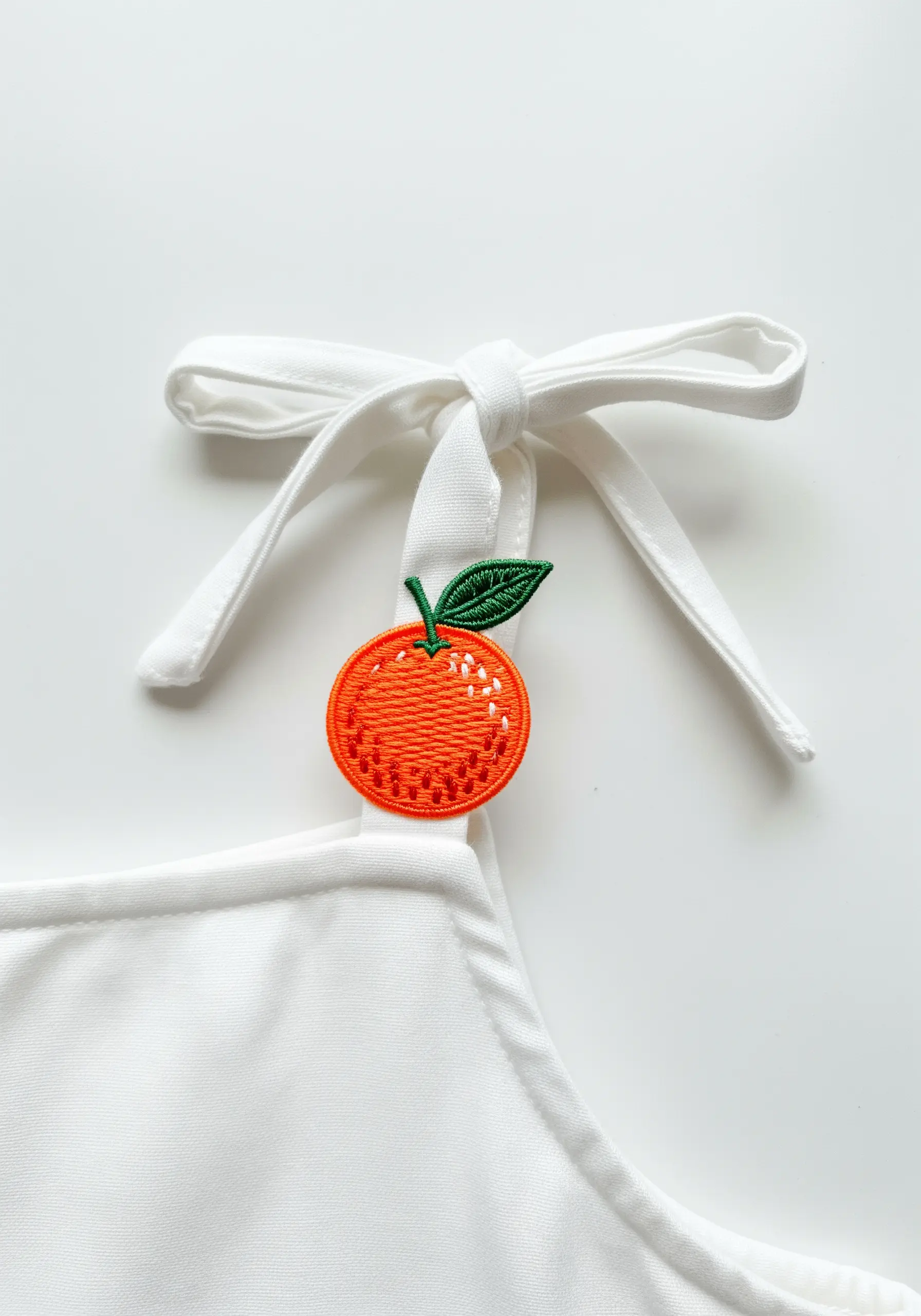 A textured orange with a green leaf embroidered on the tie of a white top.