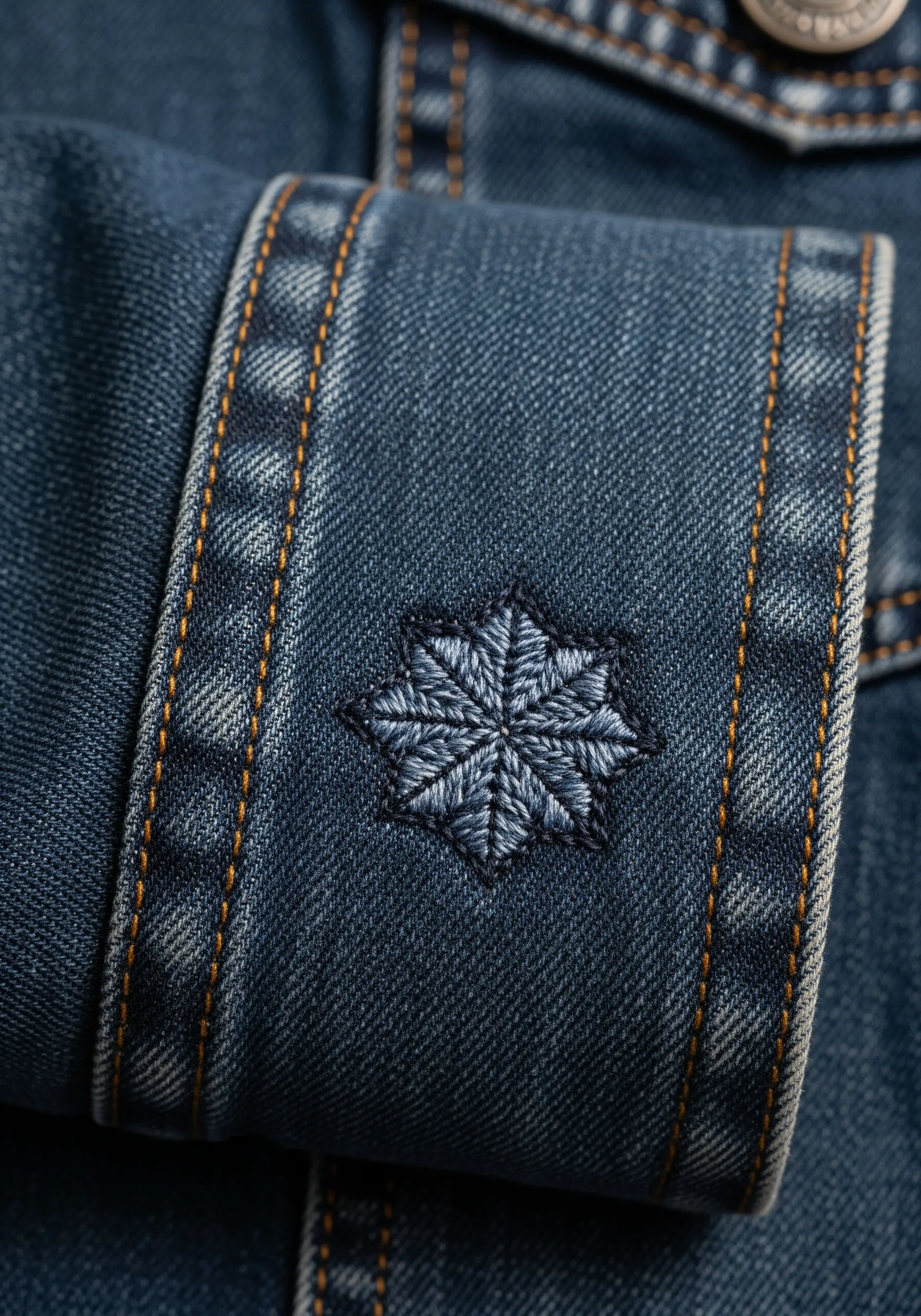 A tonal blue, star-shaped geometric motif embroidered on the cuff of a denim jacket.