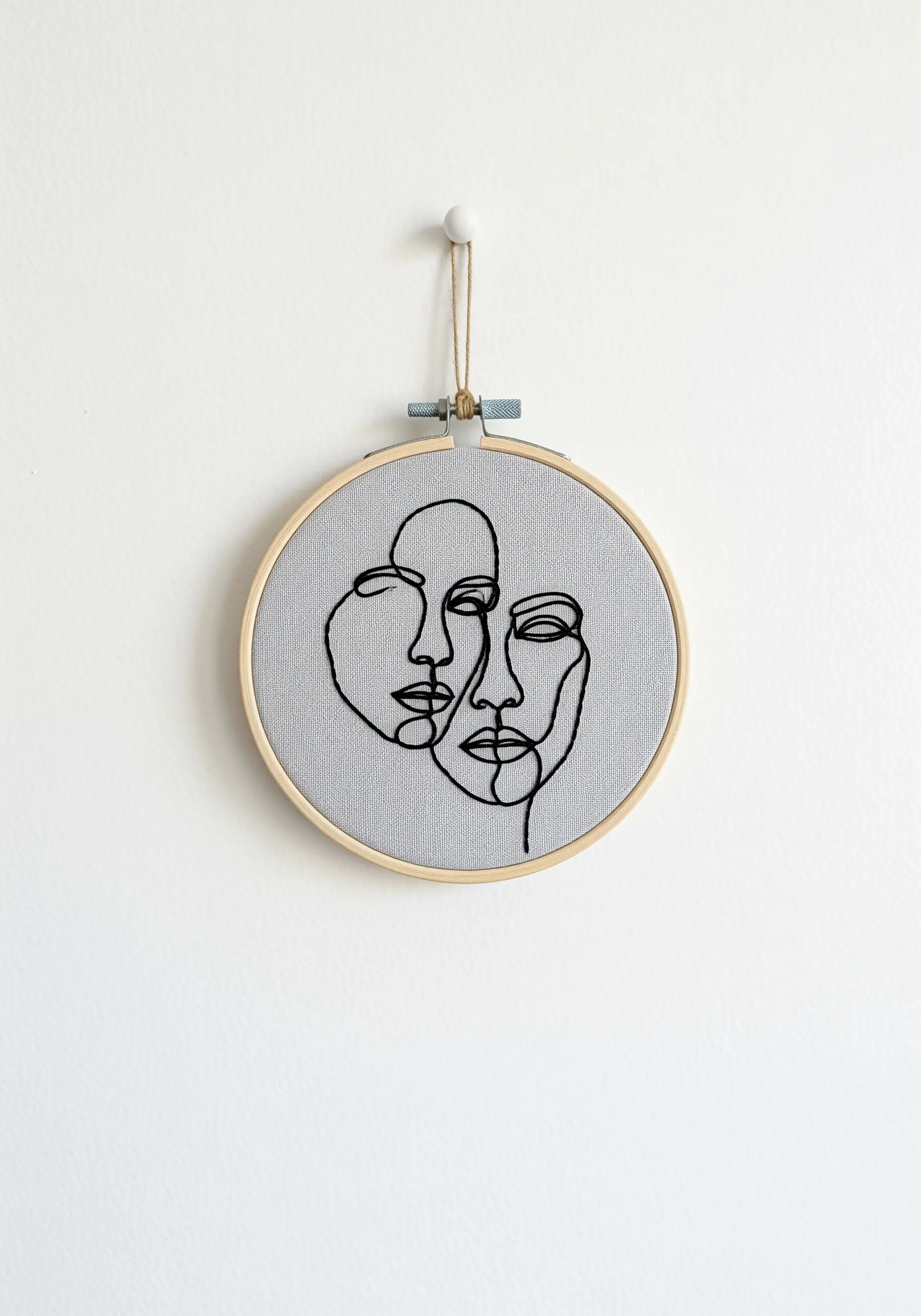 A minimalist, single-line drawing of two faces embroidered in black on gray fabric.