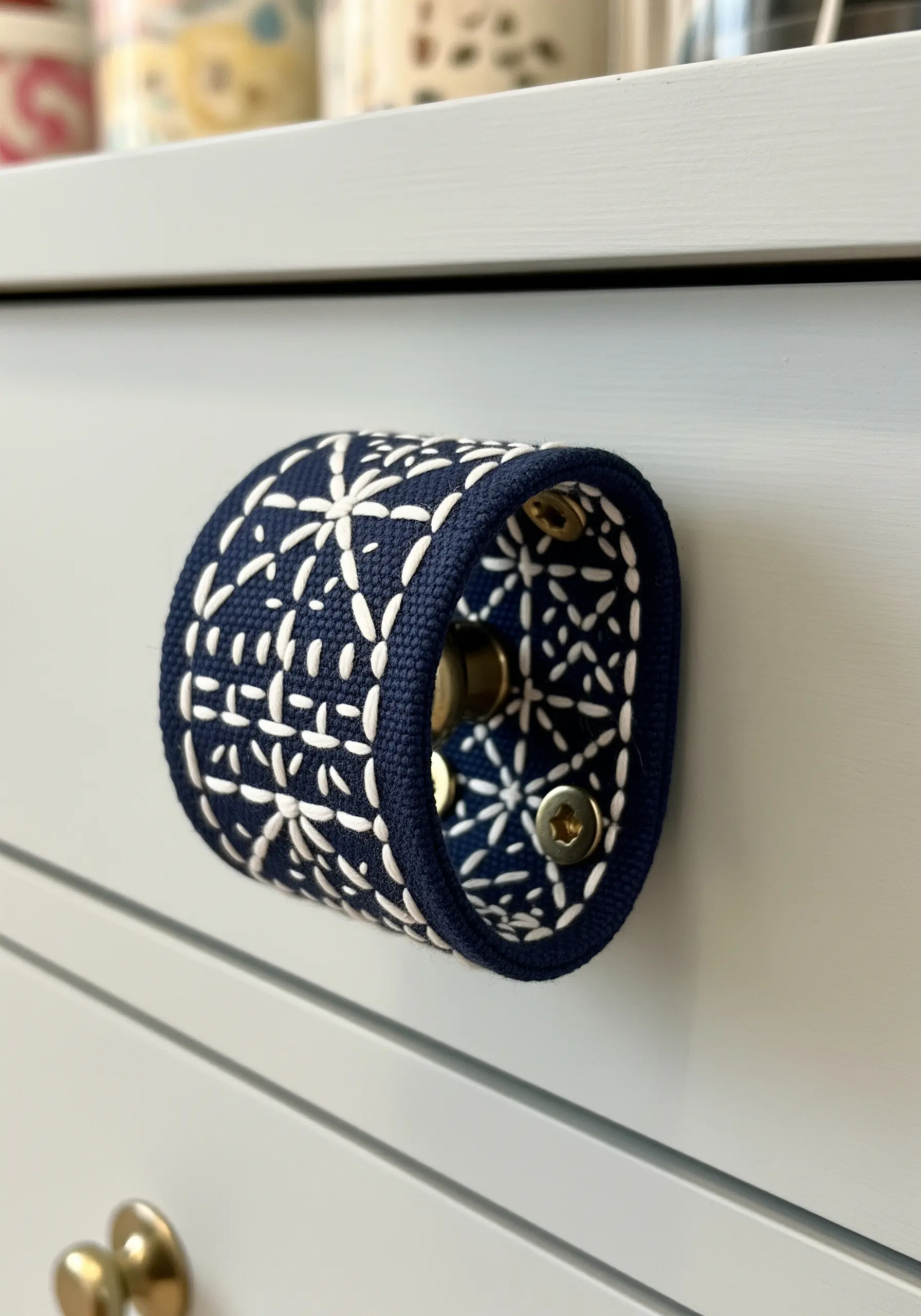 A dresser drawer pull wrapped in navy blue fabric with a white Sashiko embroidery pattern.