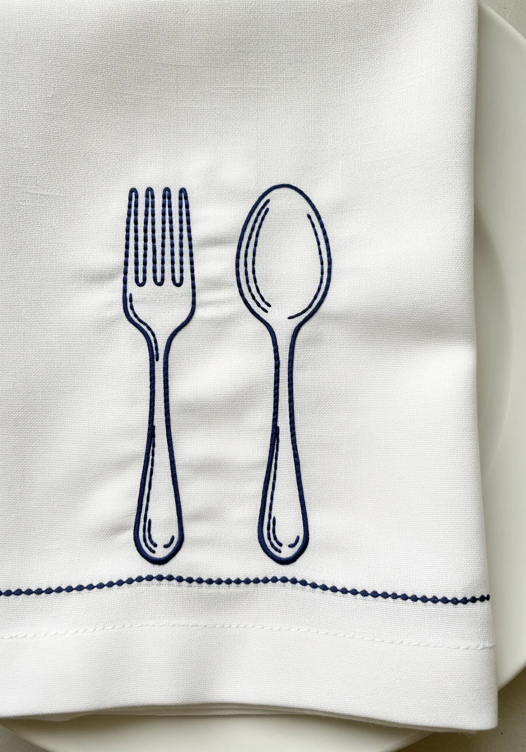 A fork and spoon embroidered in navy blue thread using a double outline technique.
