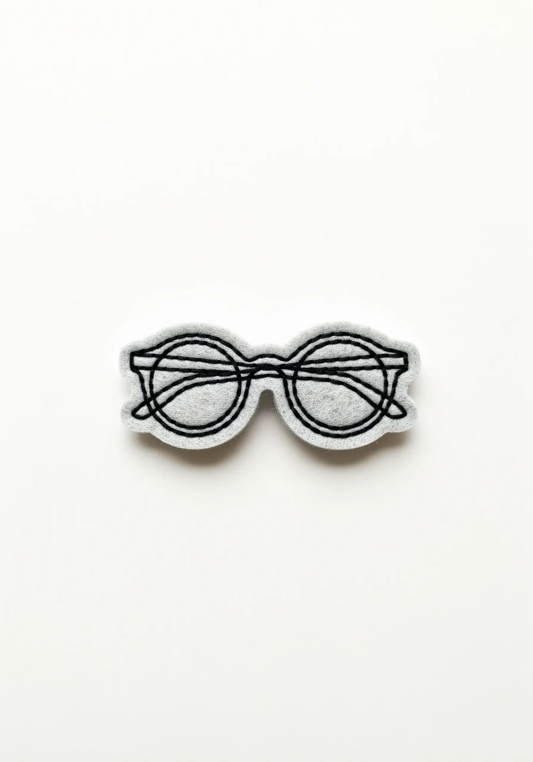A pair of glasses outlined in black backstitch on a light gray felt patch.