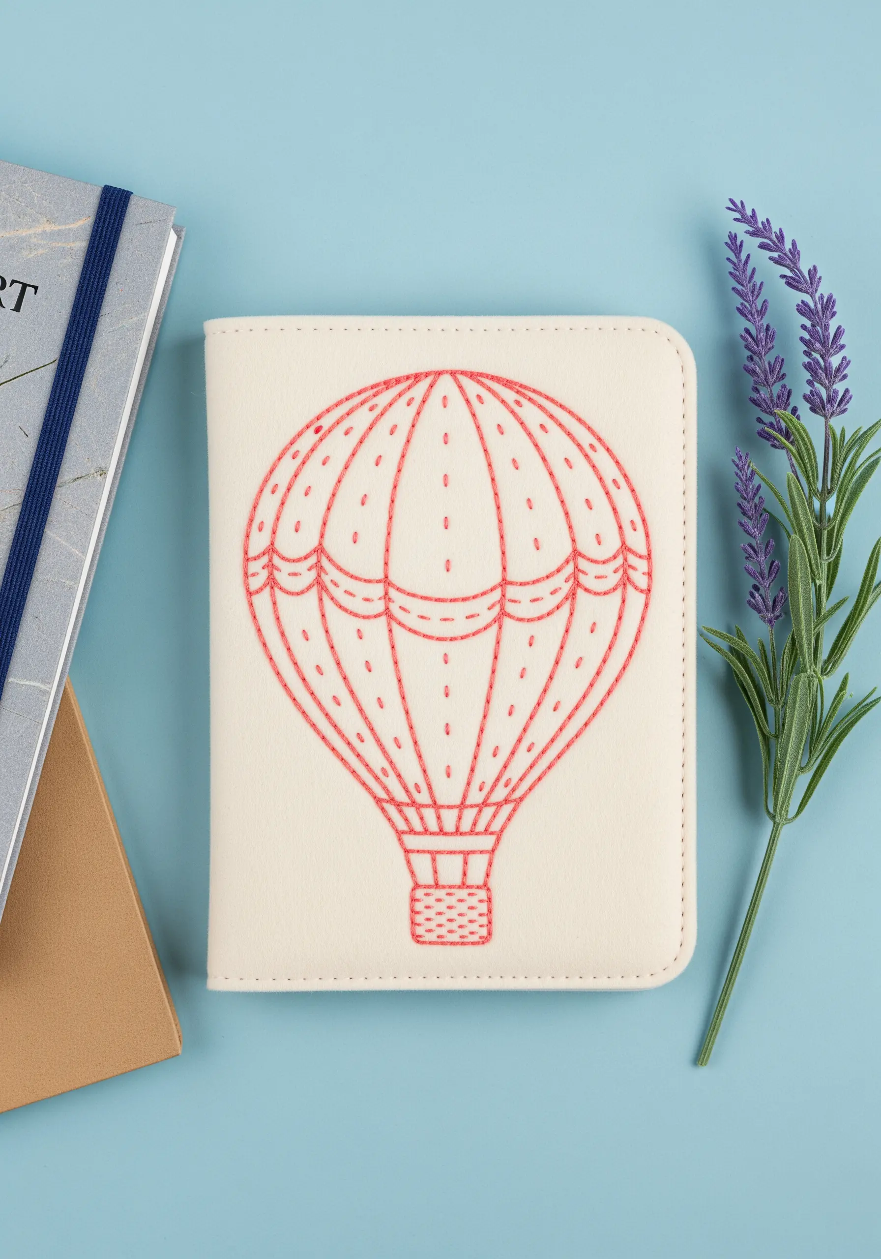 A hot air balloon outlined in coral thread on a cream passport cover, with tiny seed stitches inside.