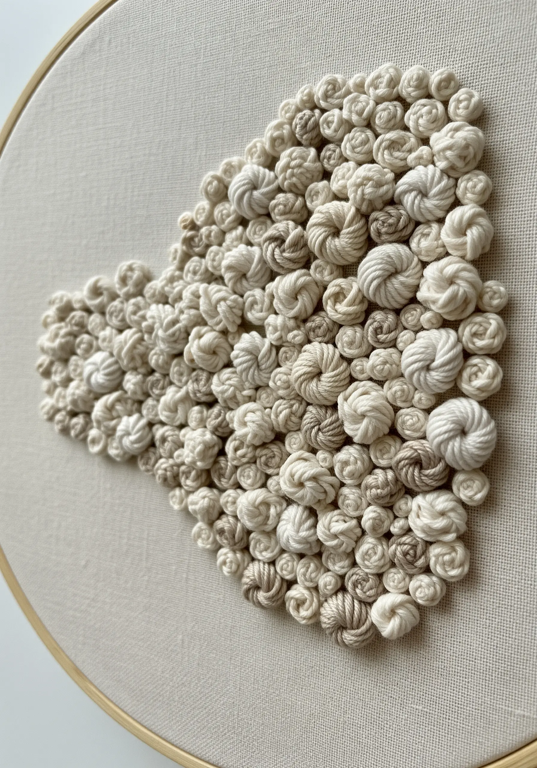 A close-up of a heart shape filled with dense, textural white and beige woven wheel stitches.