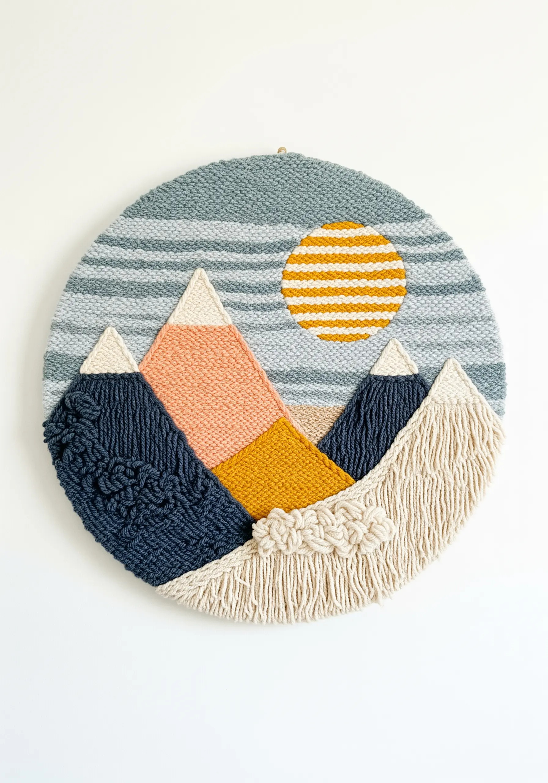 Circular woven wall hanging depicting a mountain landscape with a yellow sun.