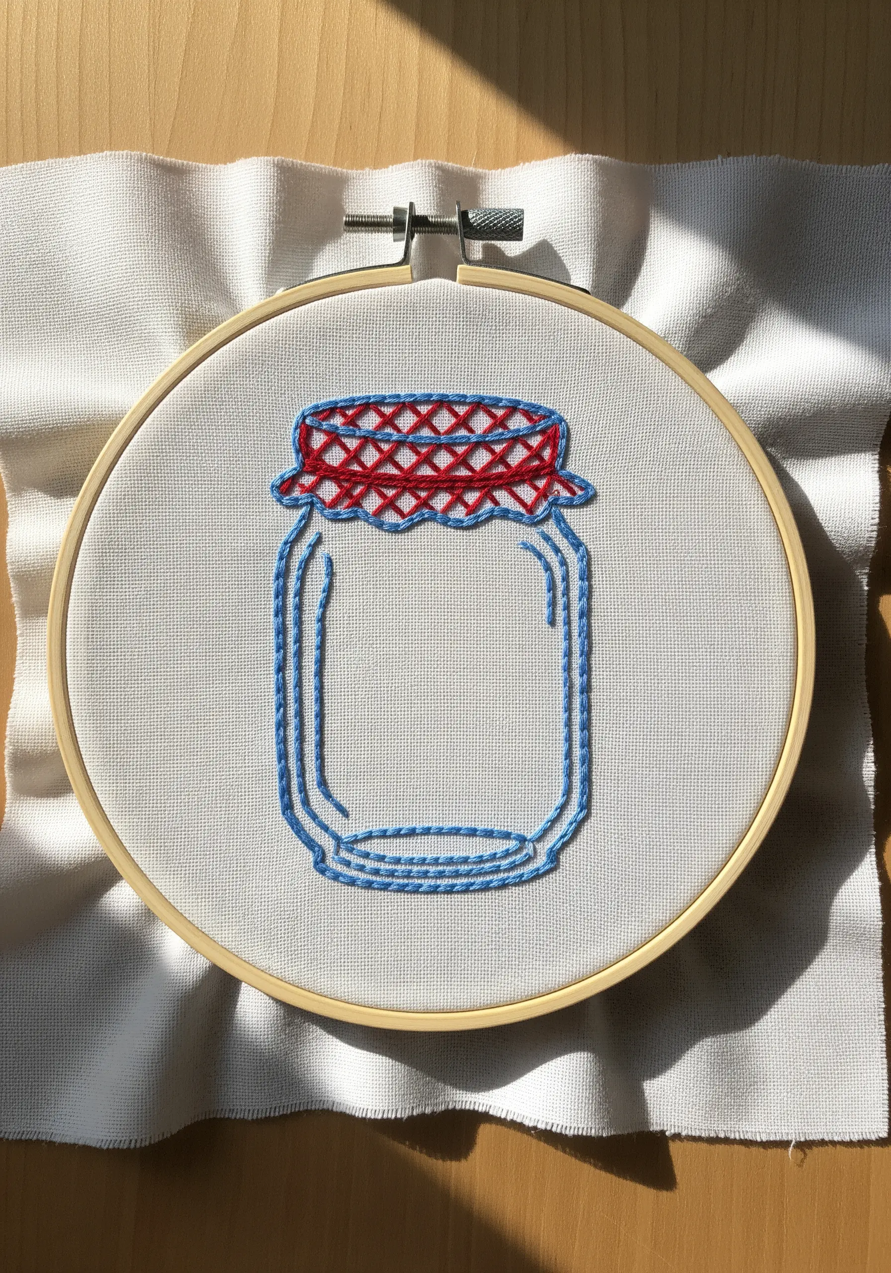 A line art embroidery of a jam jar with a red and blue woven-stitch lid.