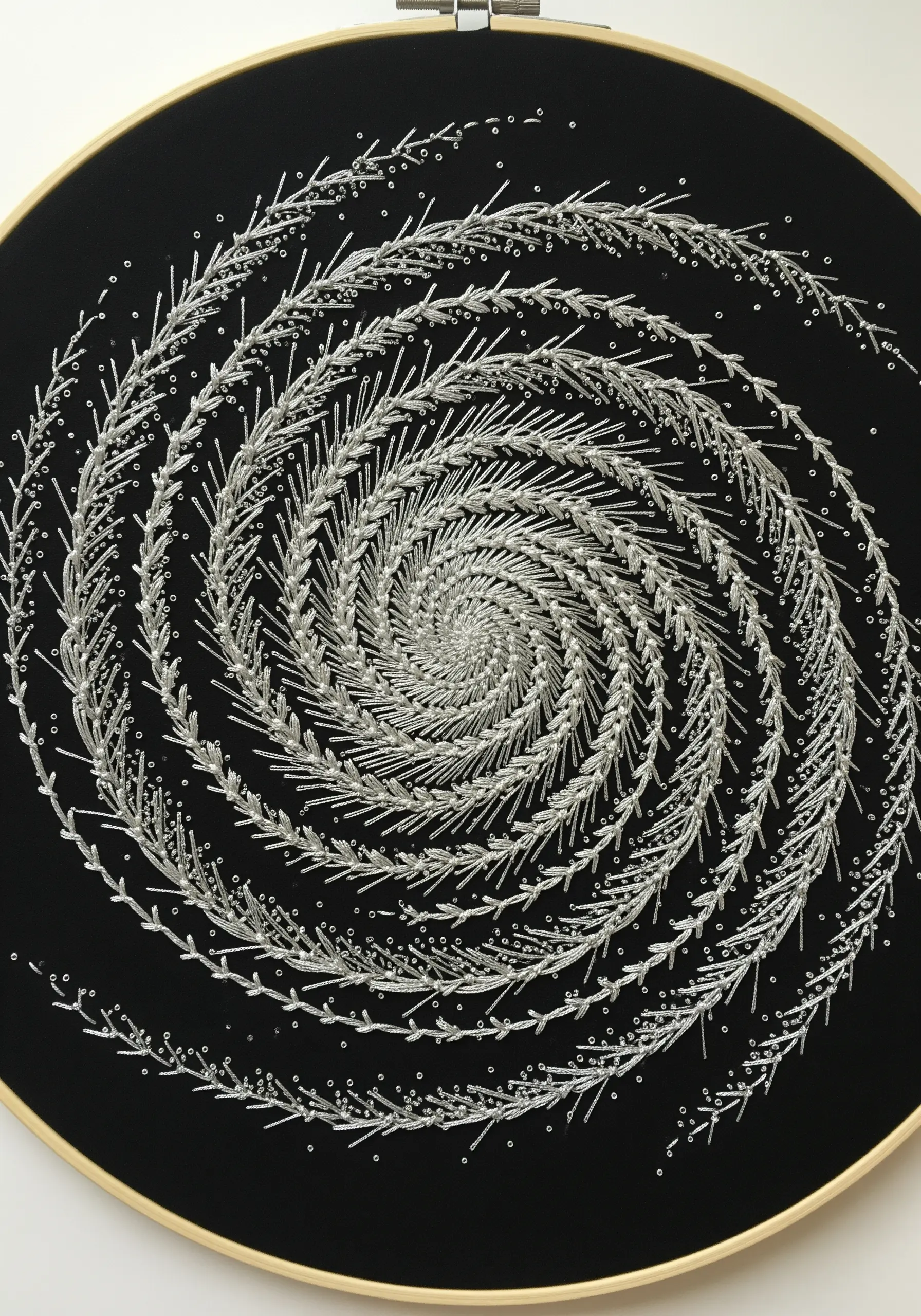 A spiral of embroidered fern stitches in silver metallic thread, accented with beads.
