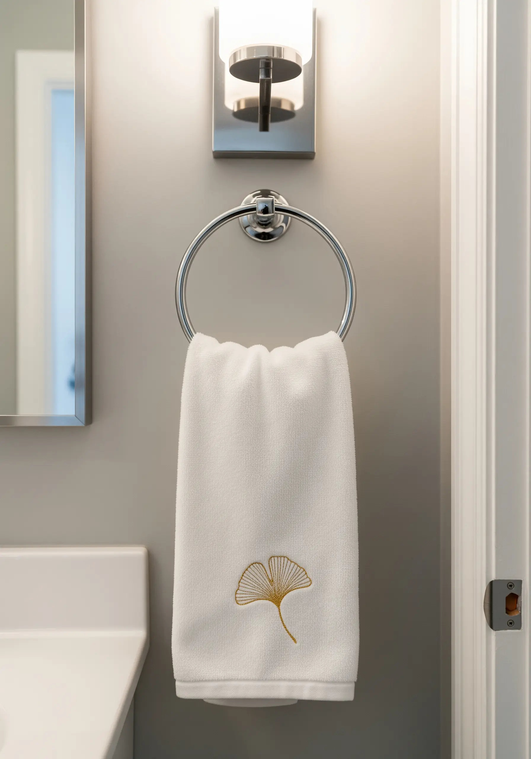 A minimalist gold metallic thread embroidery of a ginkgo leaf on a white hand towel.