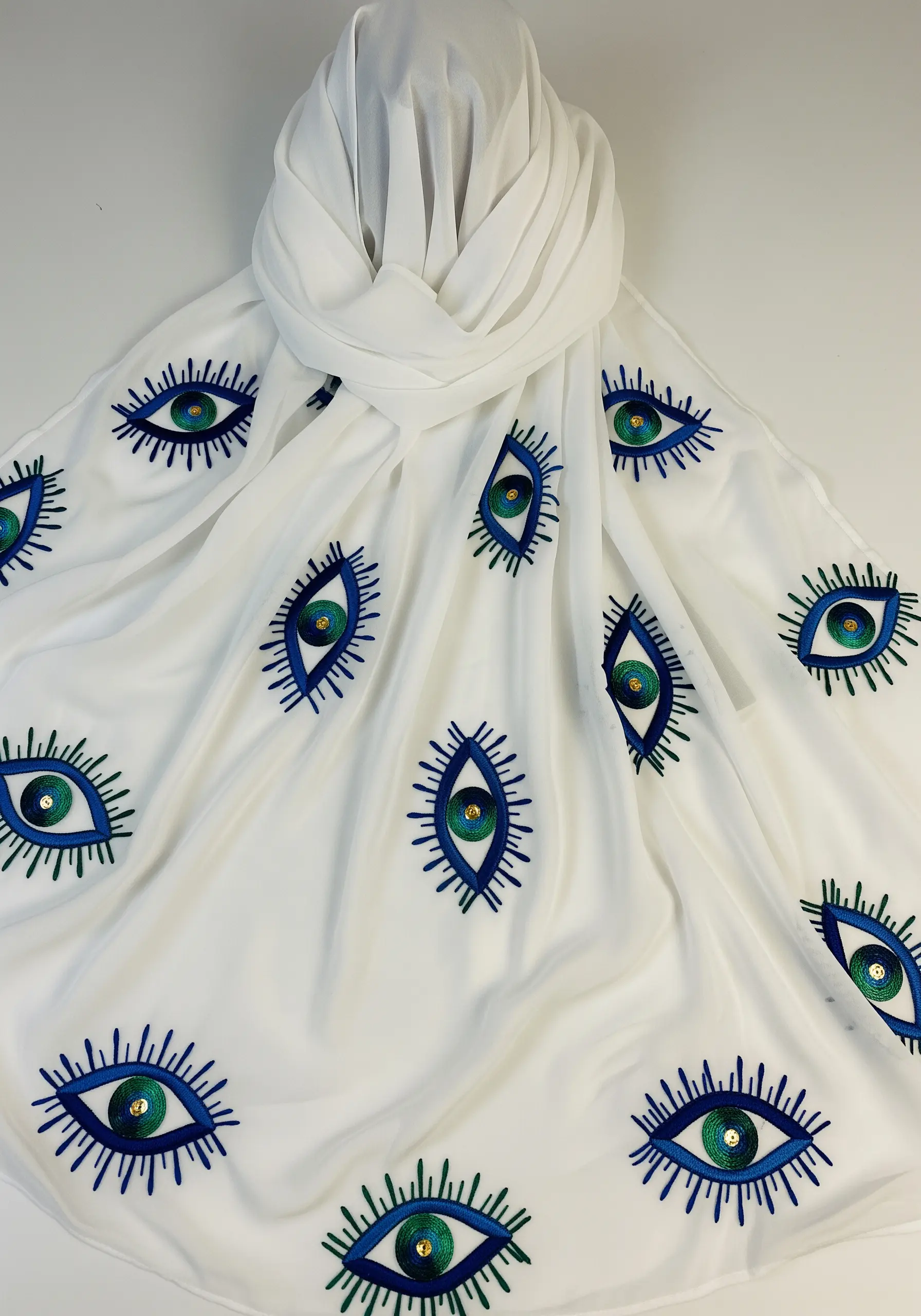 A pattern of embroidered evil eye motifs inspired by peacock feathers on a white scarf.
