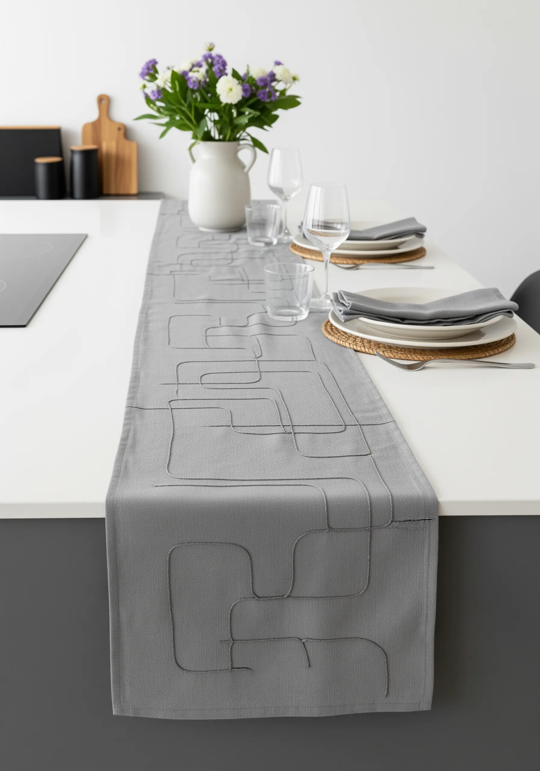 A grey table runner with a continuous, abstract black line pattern embroidered on it.