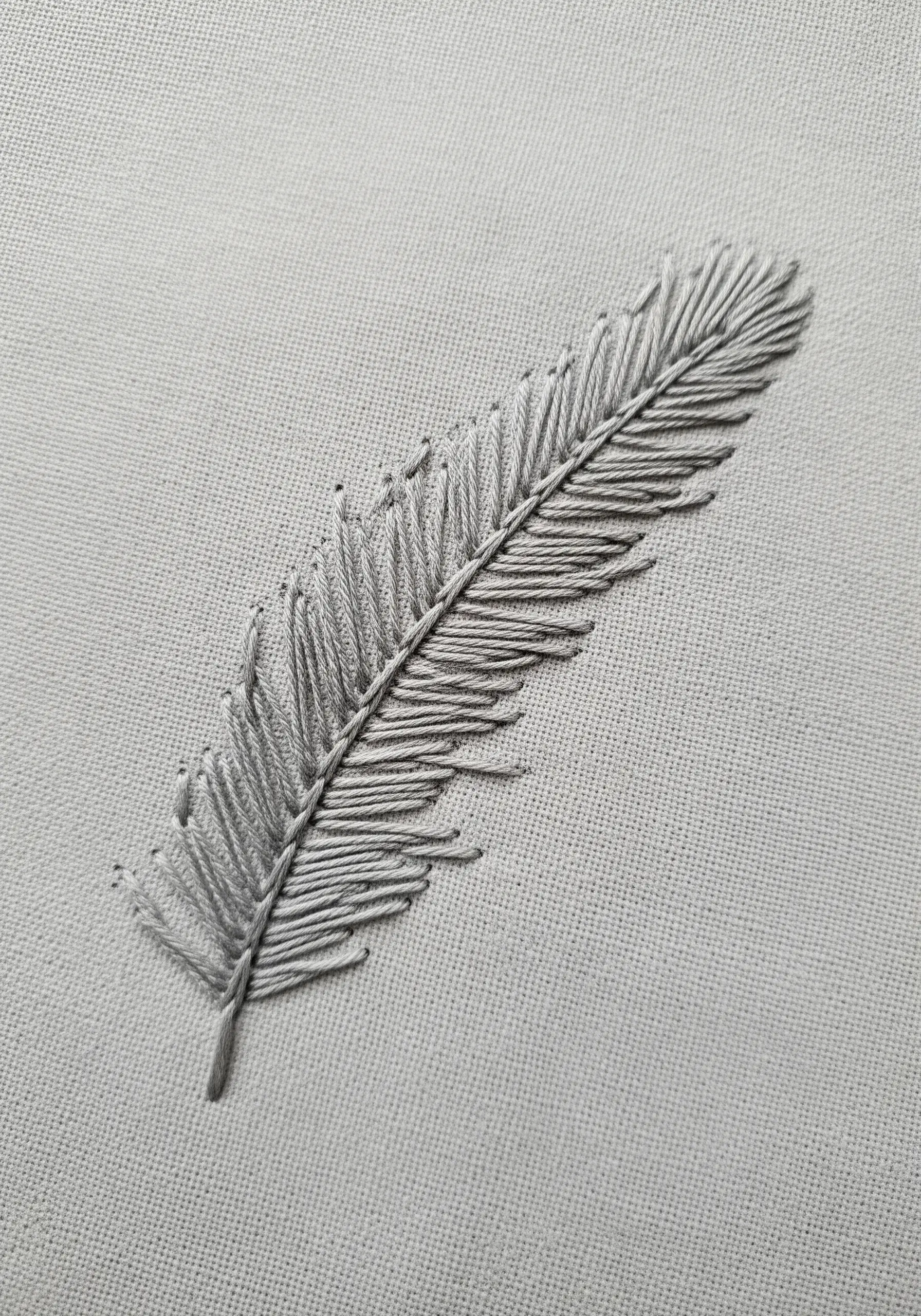 A realistic grey feather embroidered on light grey fabric using fly stitches.