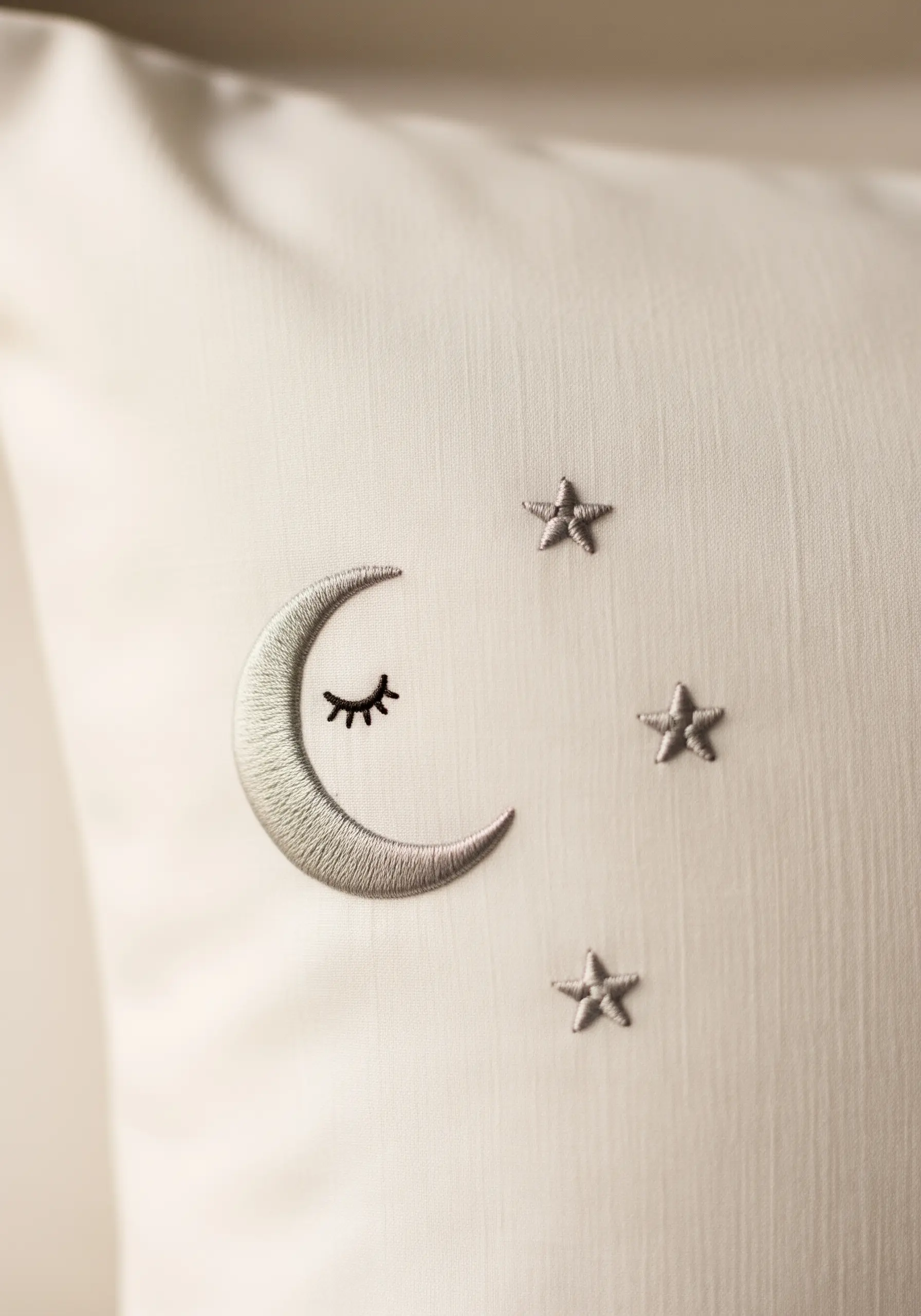 Silver satin-stitched crescent moon and stars on a white pillowcase.