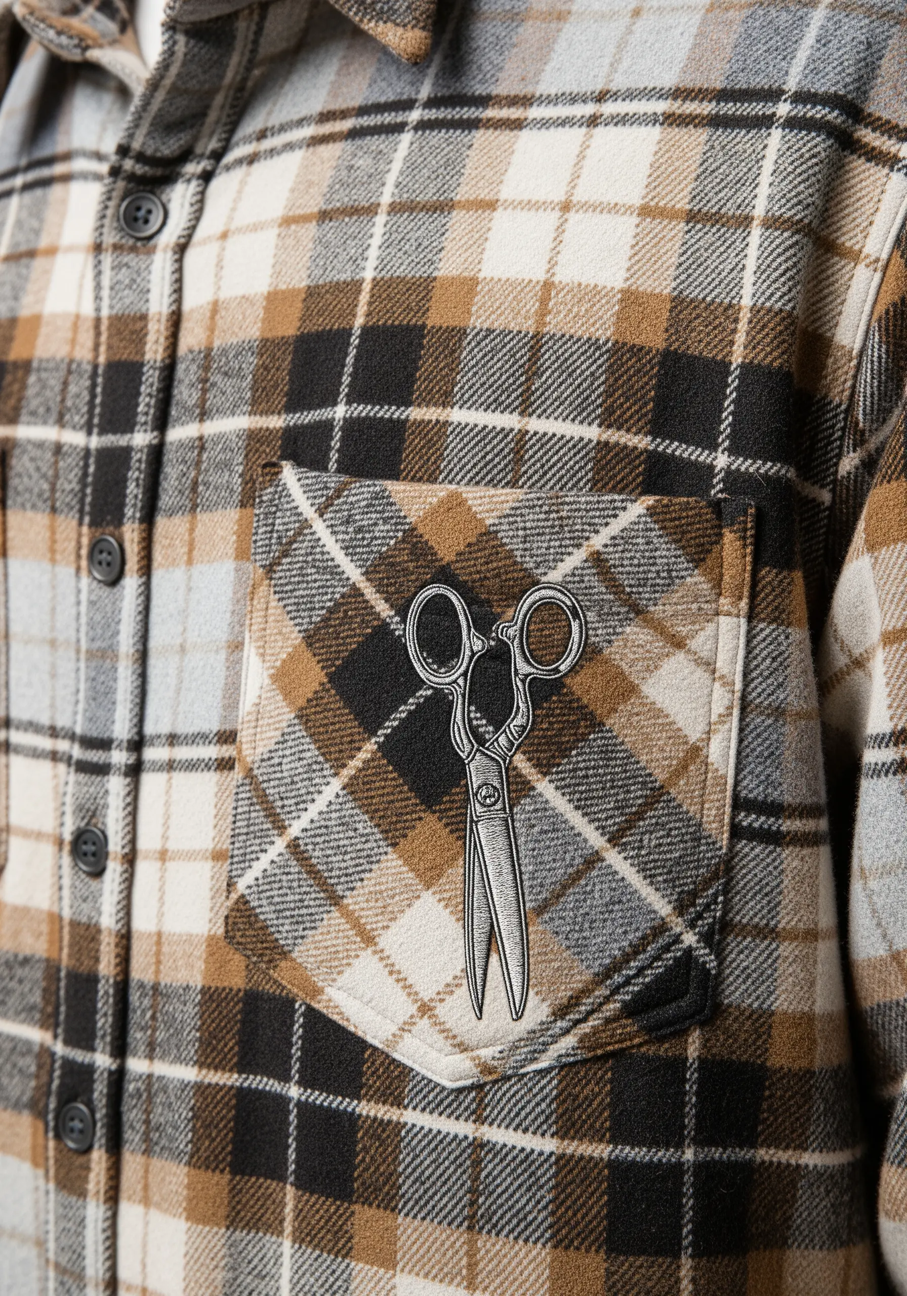 A realistic pair of vintage tailor's scissors embroidered on the pocket of a plaid flannel shirt.