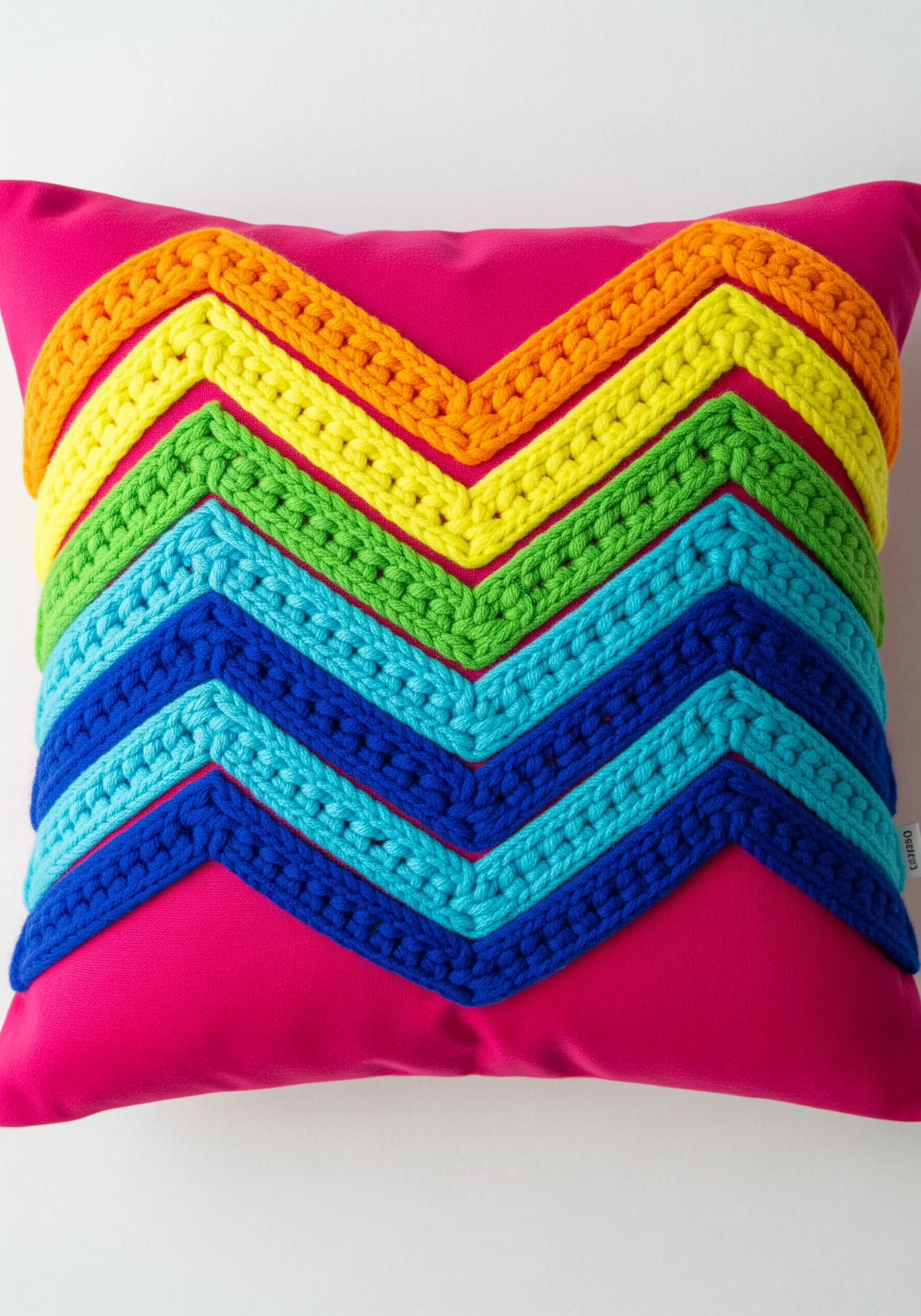 Bright rainbow chevron pattern made from crocheted yarn on a pink cushion.