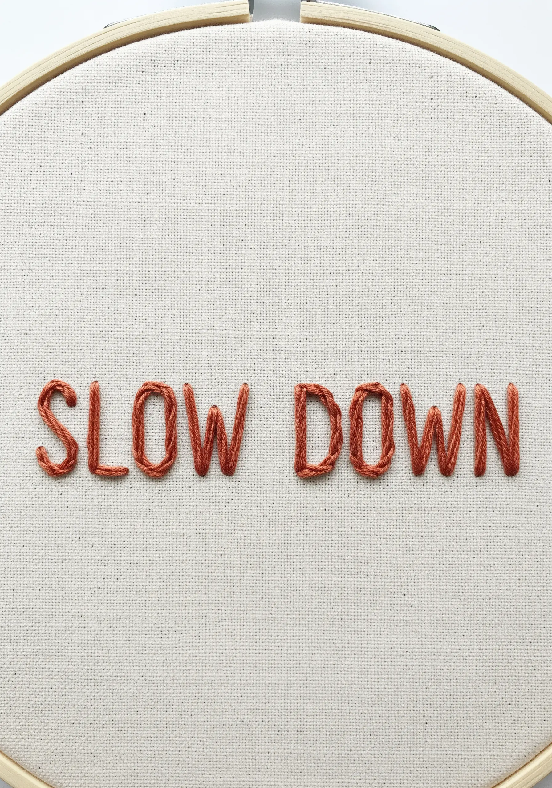 The words 'SLOW DOWN' embroidered in rust-colored backstitch on off-white fabric.