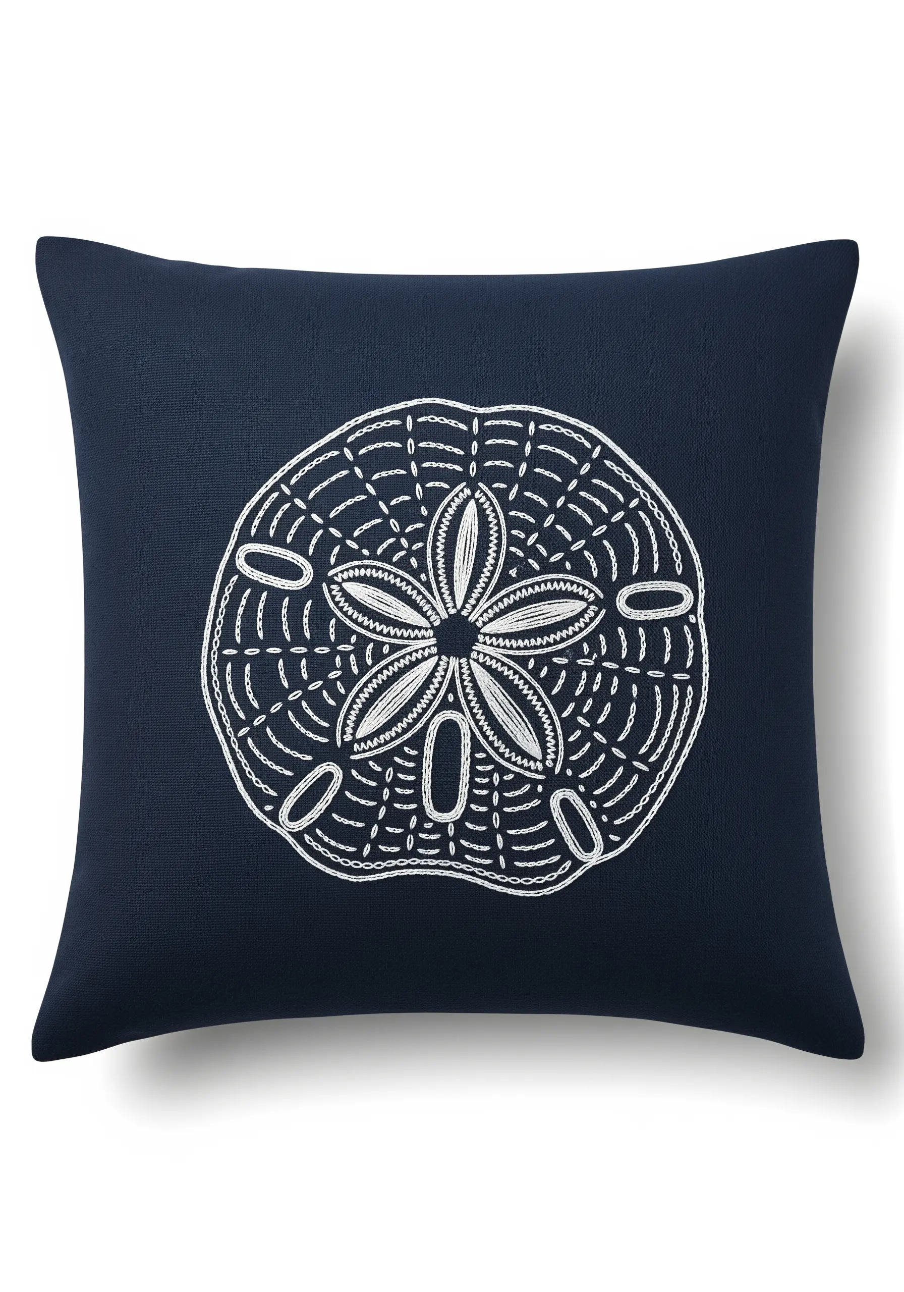 A white embroidered sand dollar design on a dark navy blue pillow