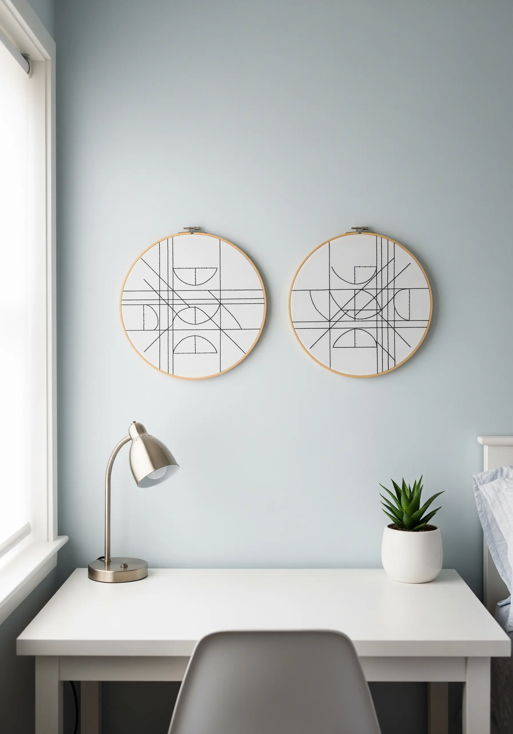 Two minimalist embroidery hoops with abstract black intersecting line art over a desk.
