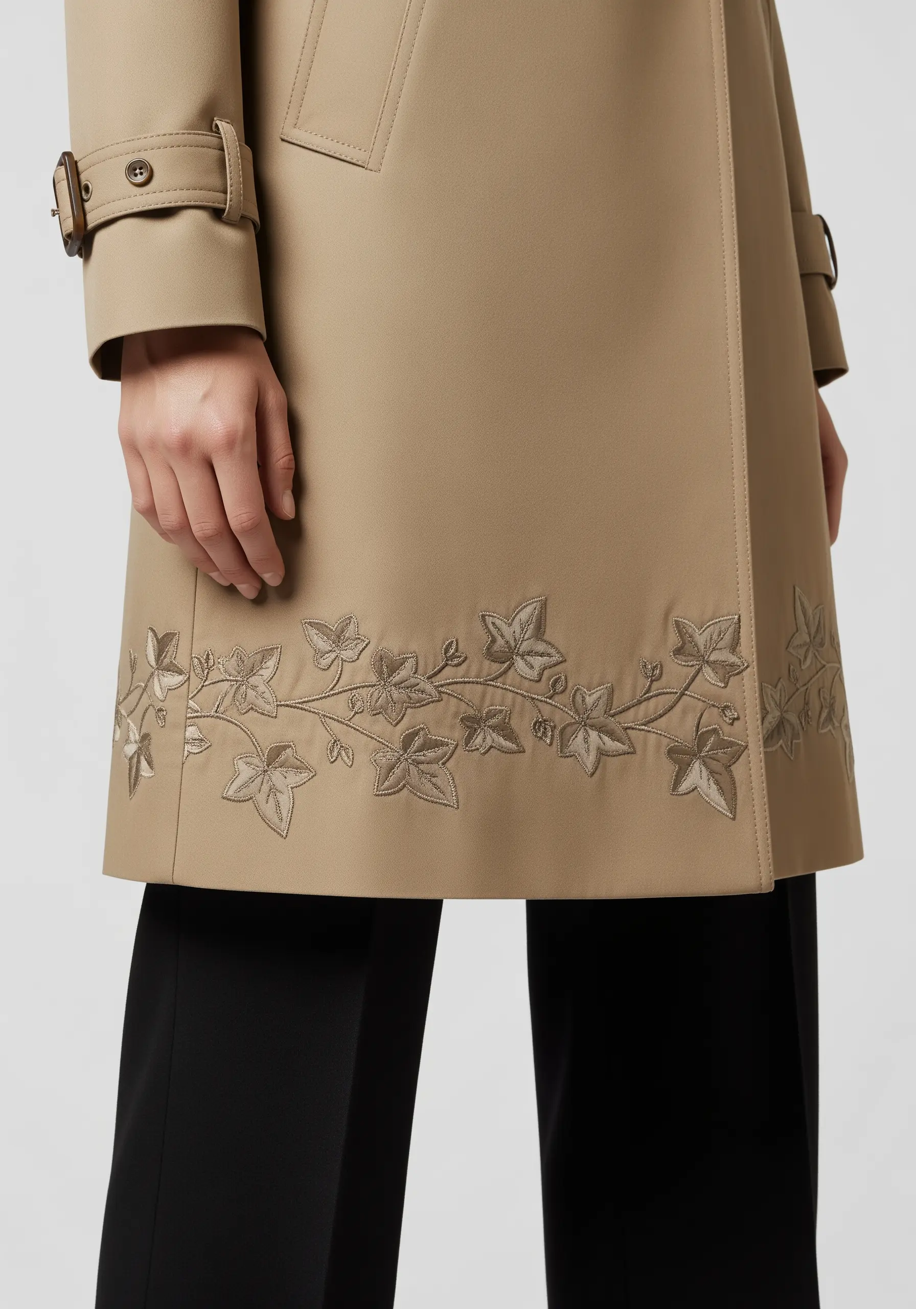 Tone-on-tone ivy leaf embroidery on the hem of a beige trench coat