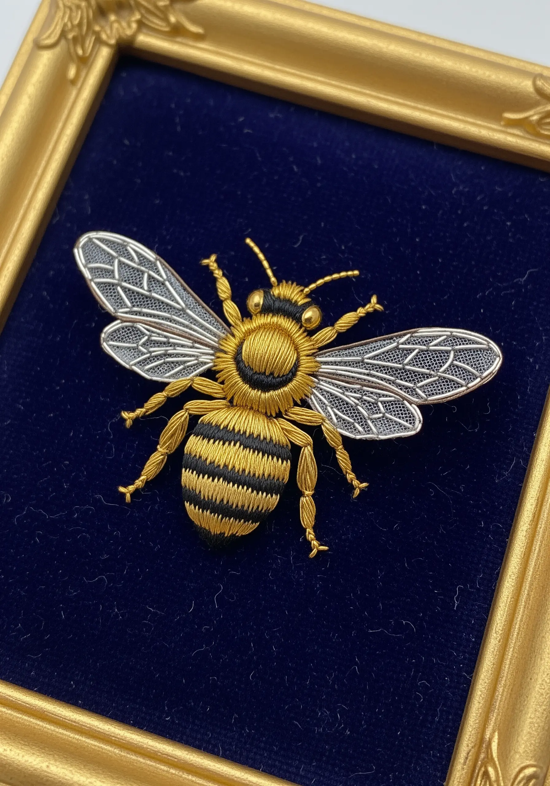 Hyper-realistic embroidered bee with gold and silver thread on dark blue velvet.