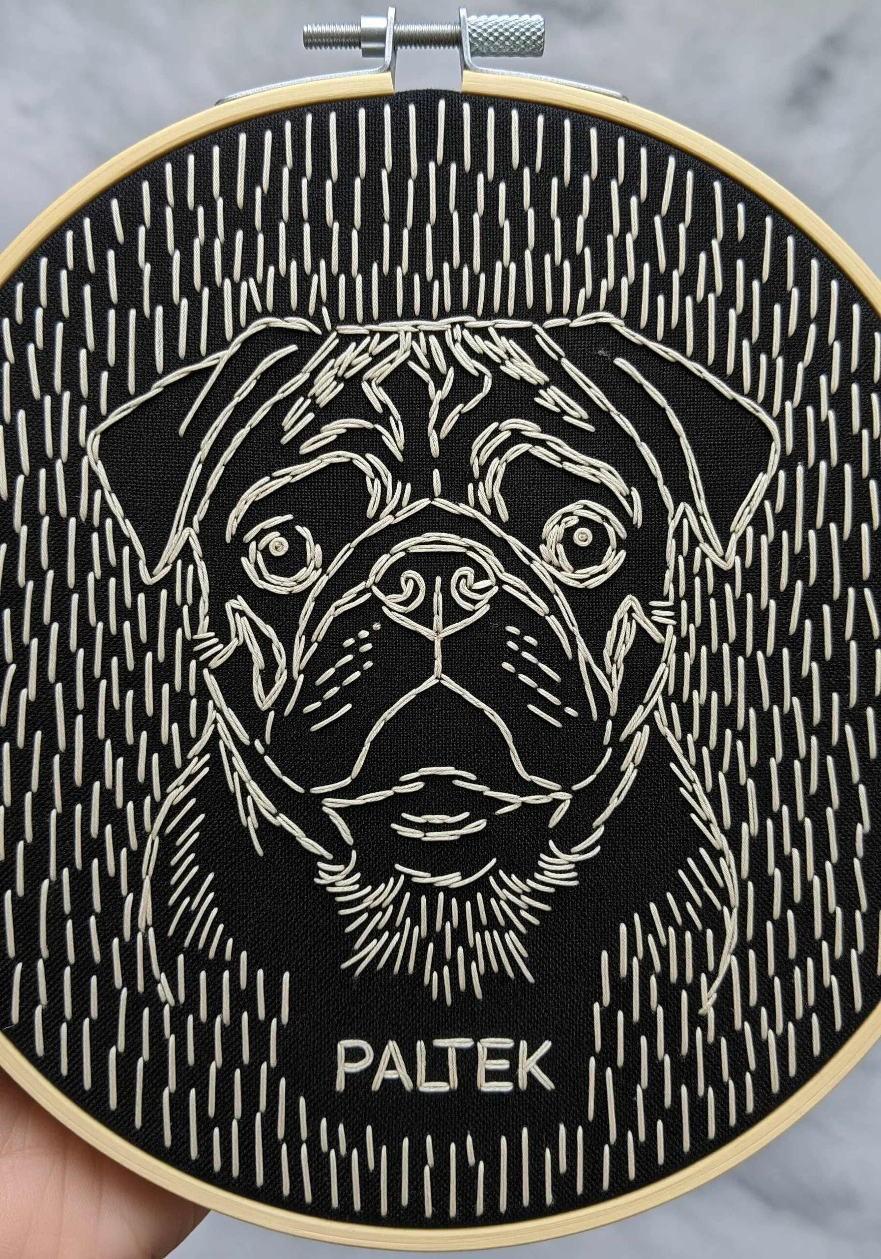A line art pug portrait with a background of vertical white stitches on black fabric.