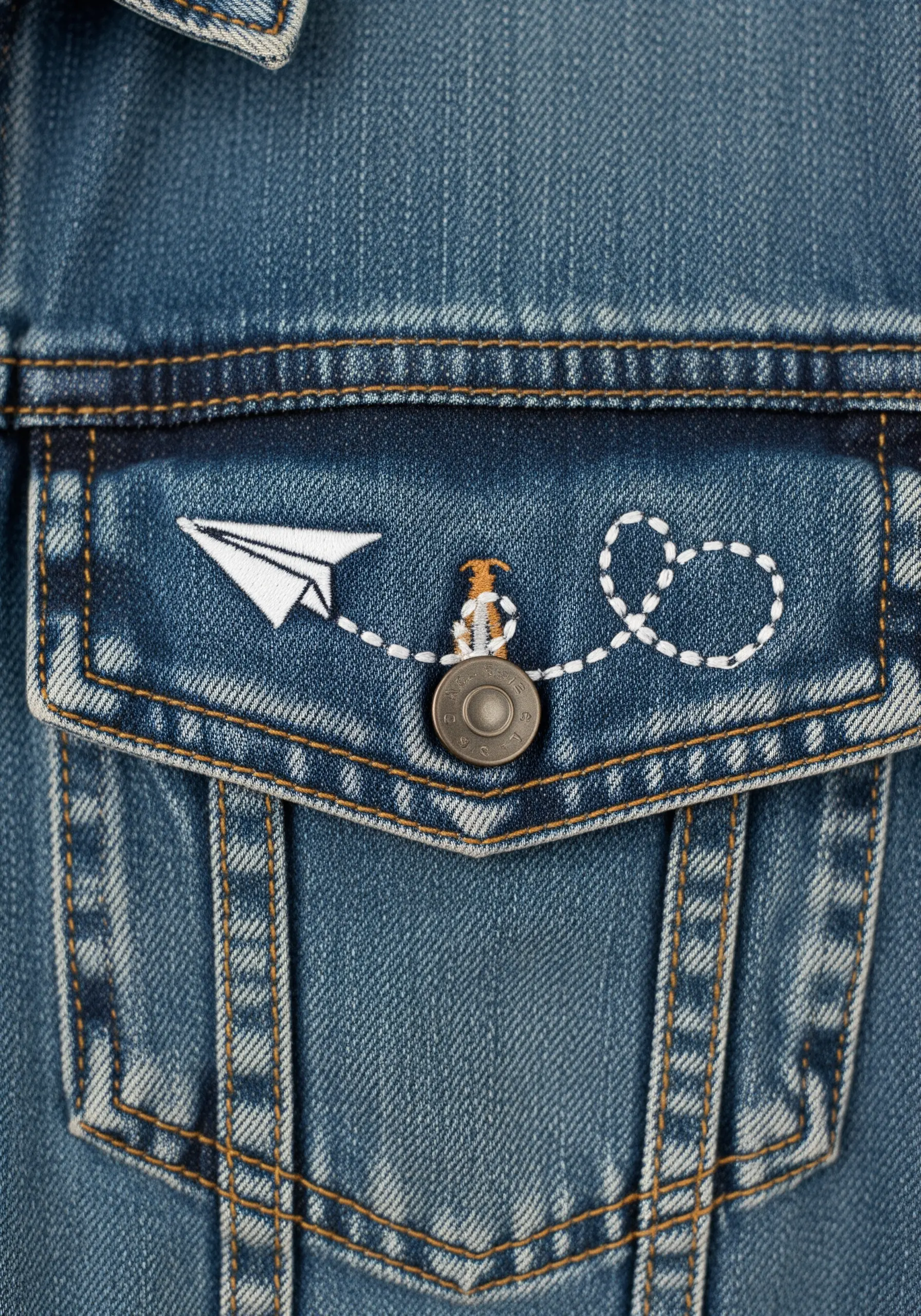 A tiny paper airplane and a stitched flight path embroidered on a denim jacket pocket.