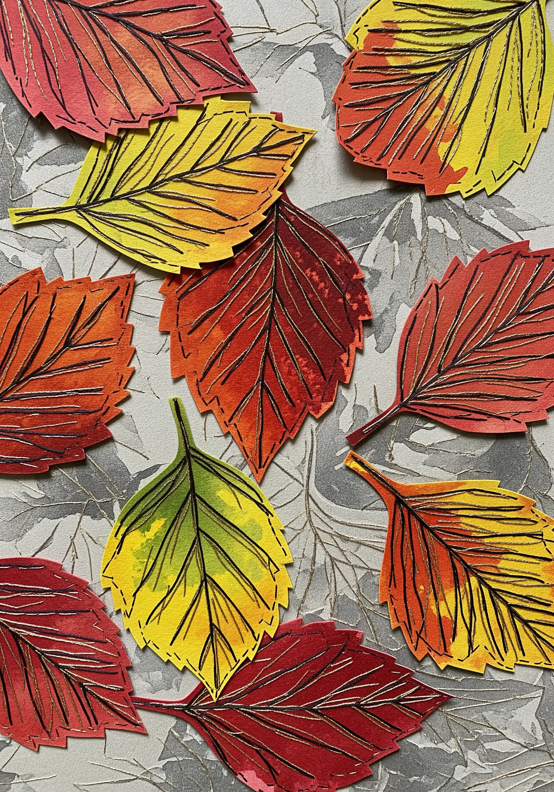Autumnal leaves cut from watercolor paper with veins stitched in black thread.