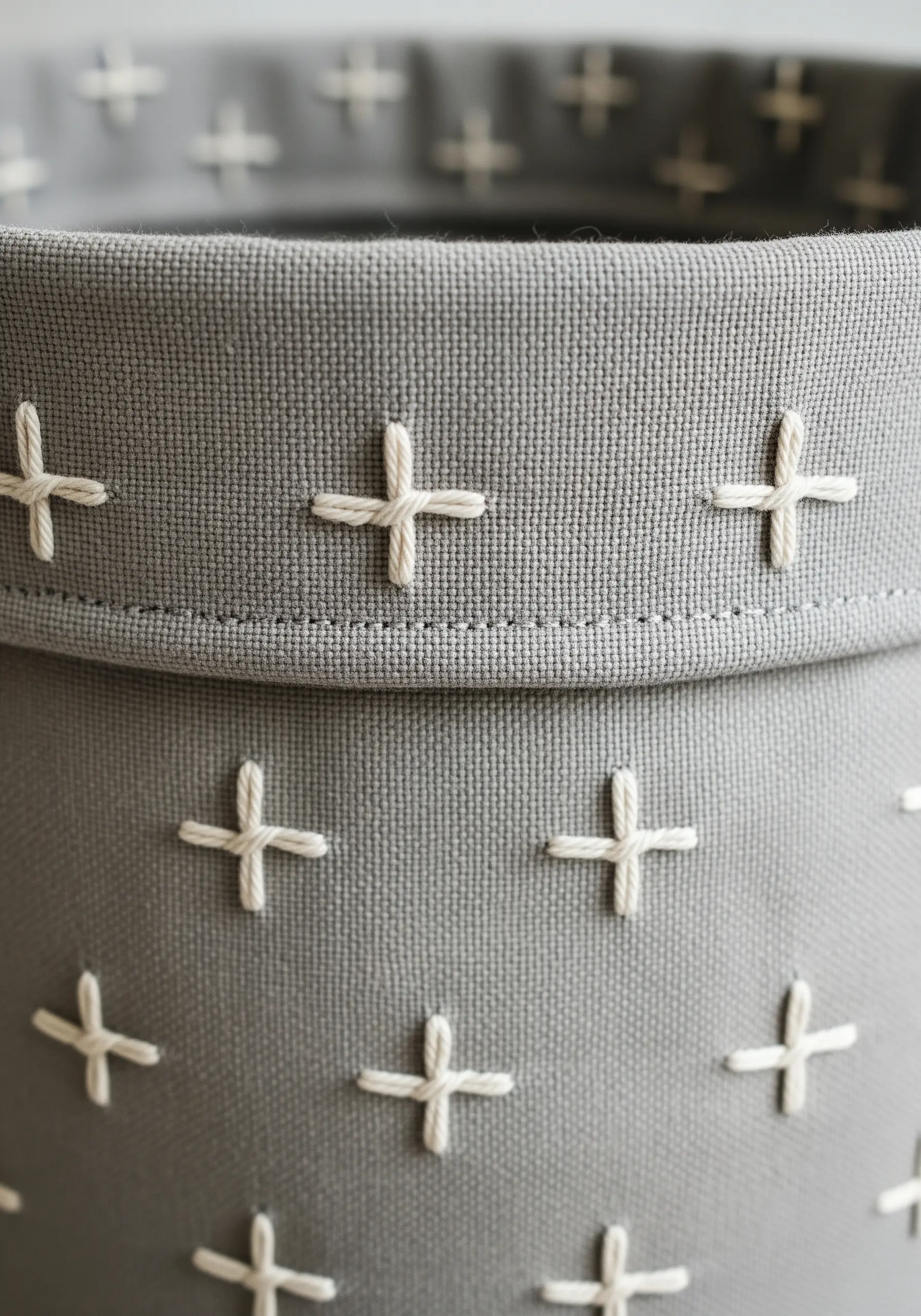 Detail of a grey fabric basket decorated with a pattern of white cross stitches.