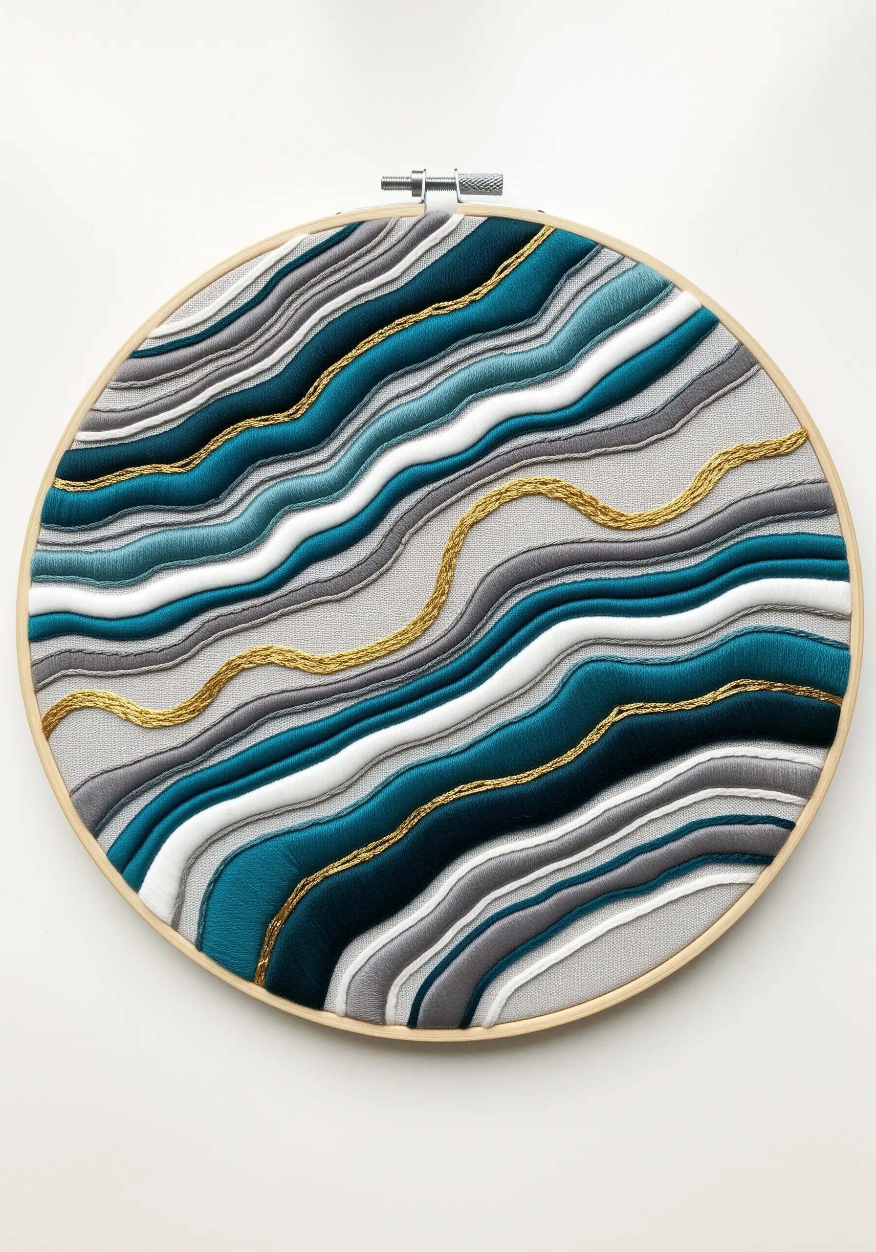 Abstract hoop art with wavy, layered bands of satin stitch in teal, gray, and gold, resembling an agate slice.