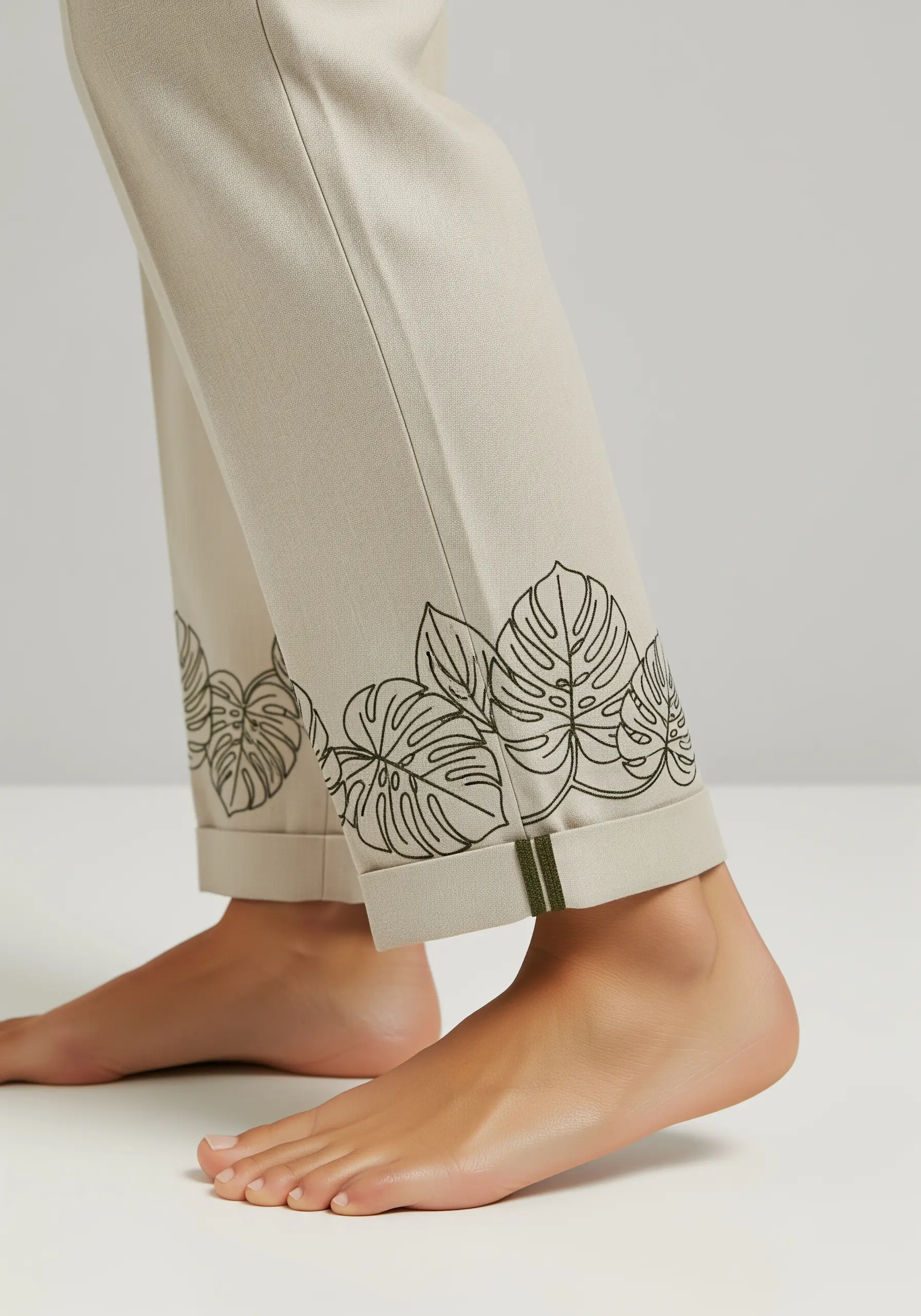 Minimalist line art of Monstera leaves embroidered on the rolled cuff of beige trousers