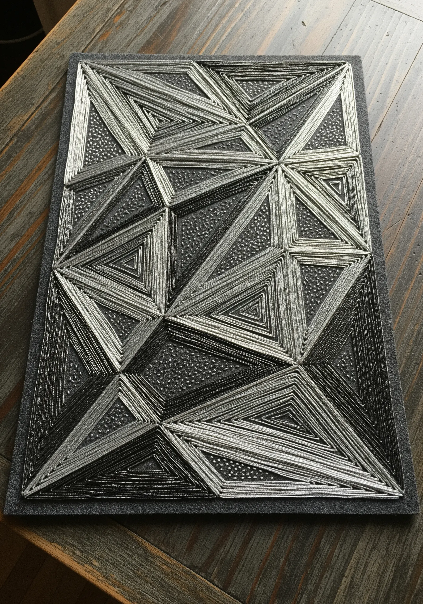 Geometric string art embroidery with layered metallic silver triangles on gray felt.