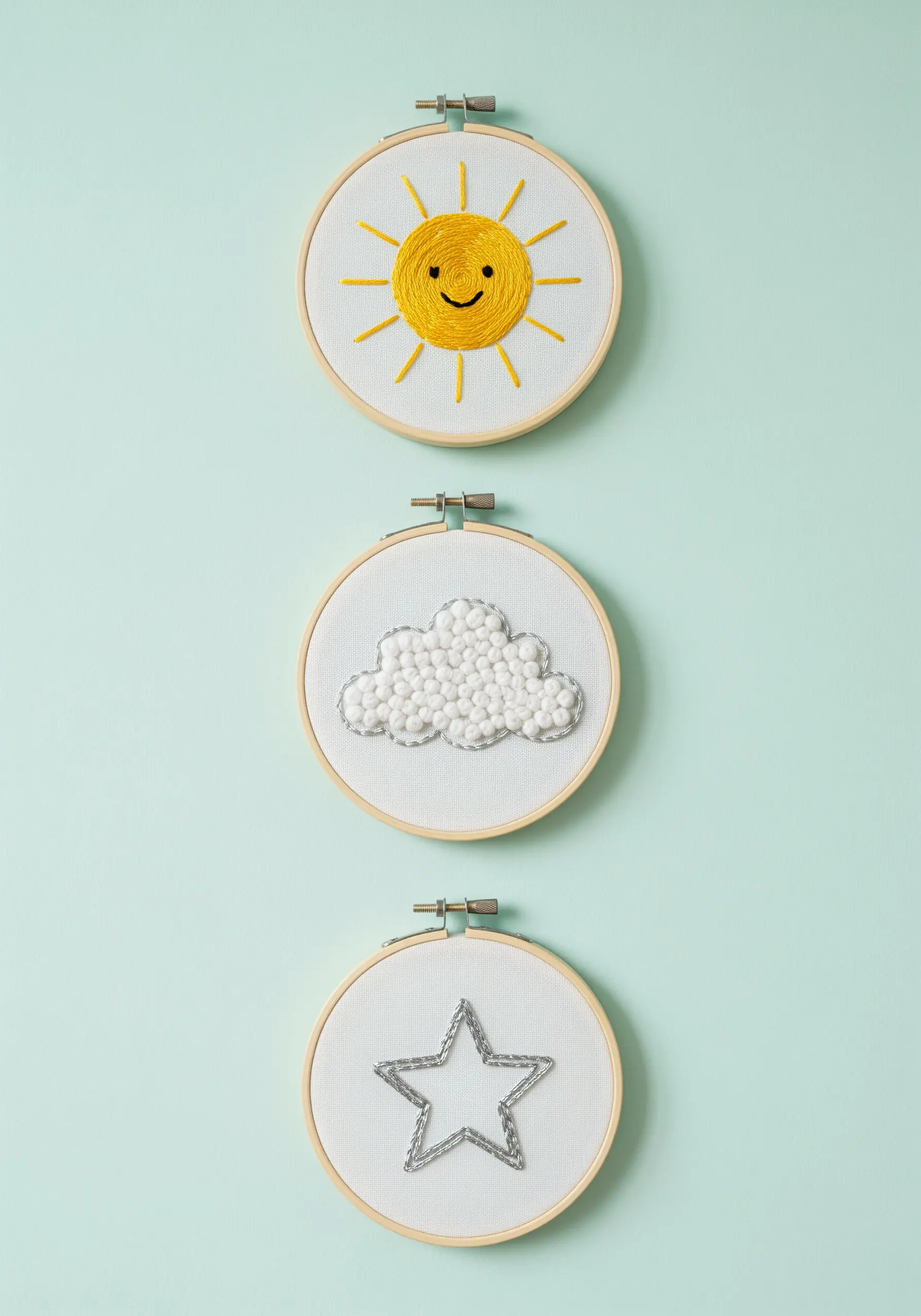 Three embroidery hoops: a satin-stitched sun, a French knot cloud, and a metallic star.