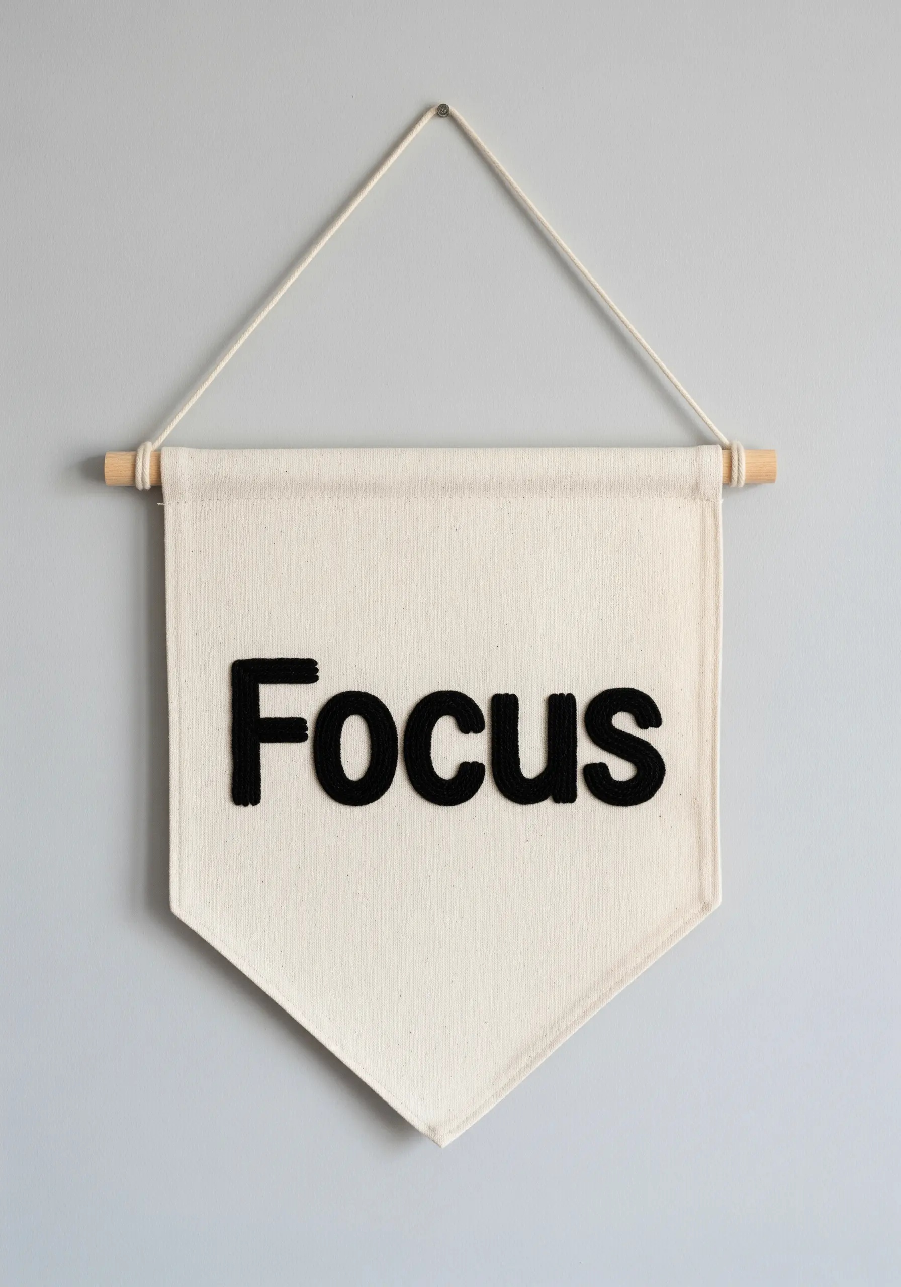 A canvas wall banner with the word 'Focus' in thick, raised black embroidery.