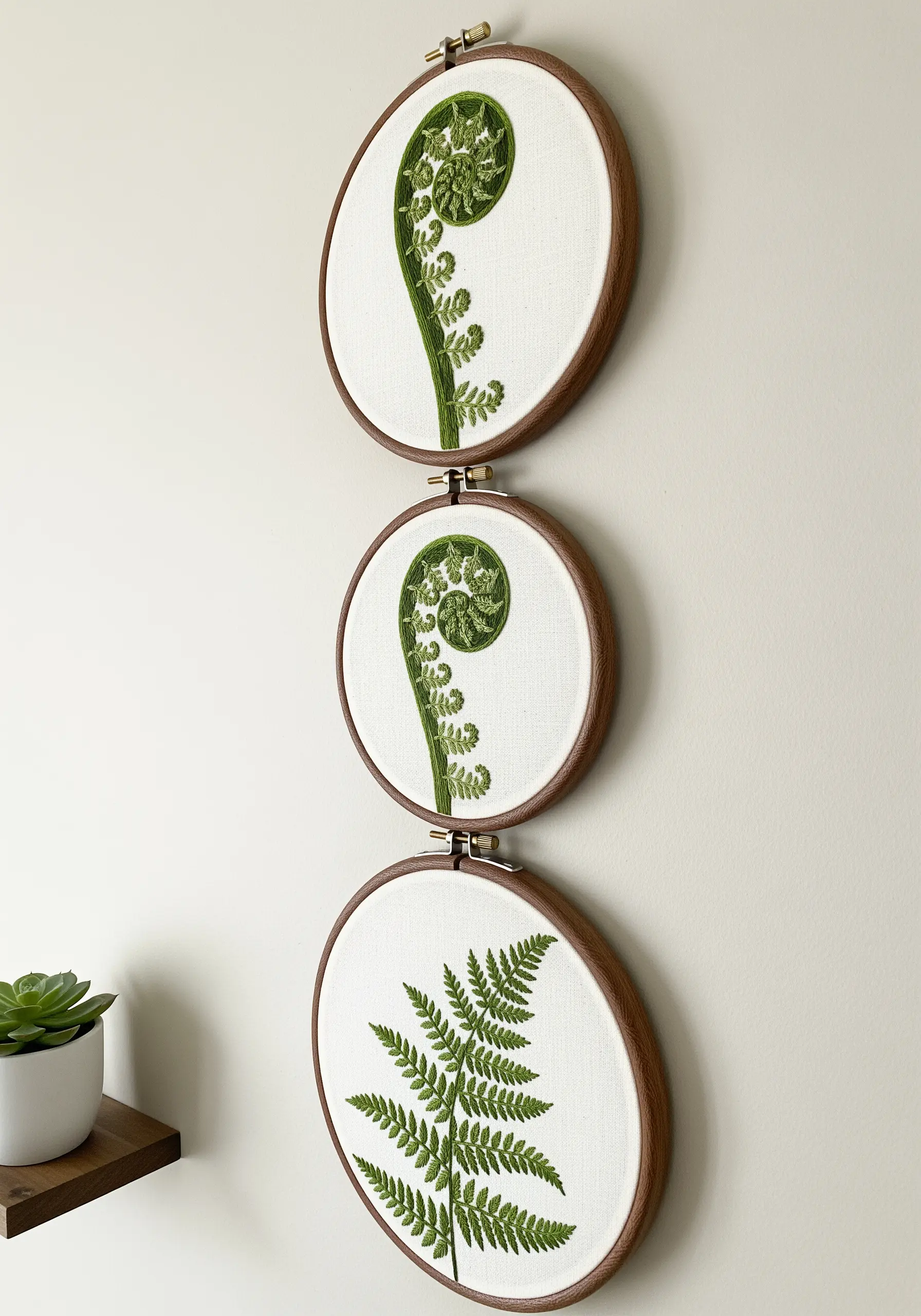 A triptych of embroidery hoops showing the growth stages of a fern.