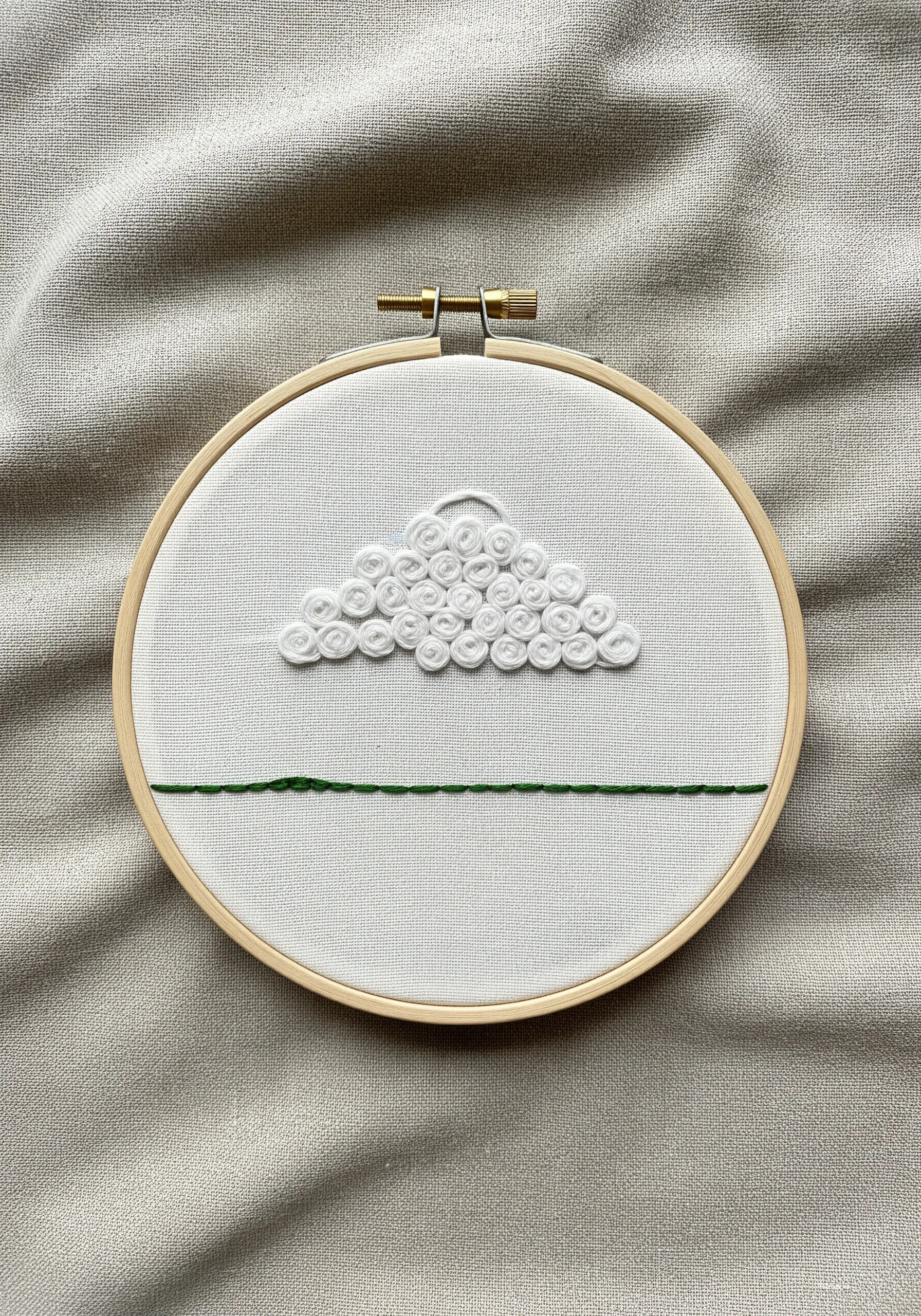 Stylized cloud embroidered with white French knots above a simple green horizon line.