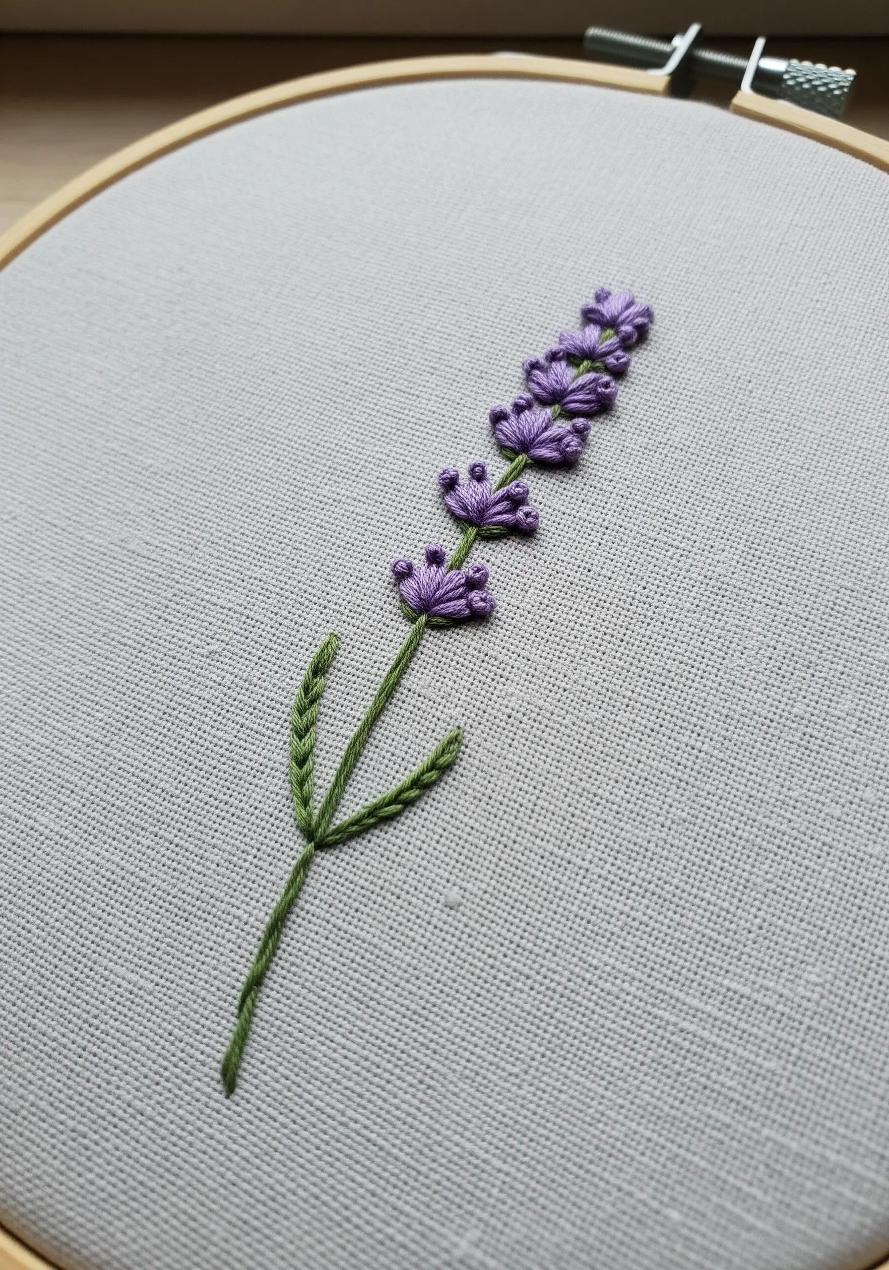 An embroidered lavender sprig using woven wheel stitches for flowers and fishbone stitch for leaves.