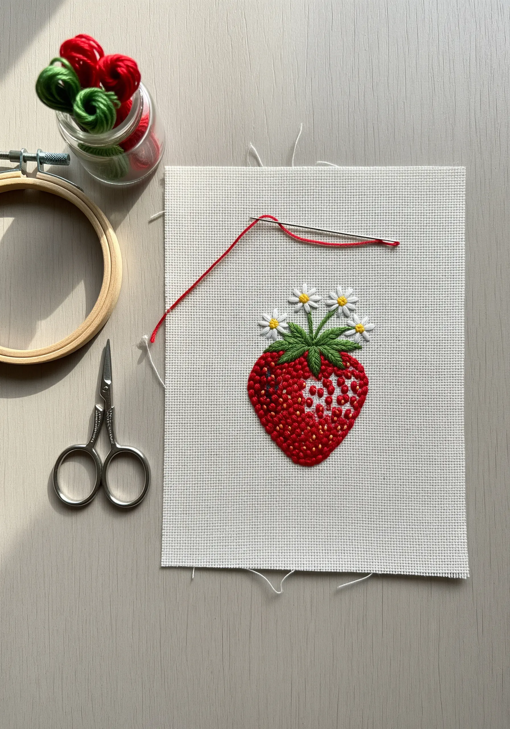 A plump red strawberry with white daisy flowers, embroidered with textural French knots for seeds.