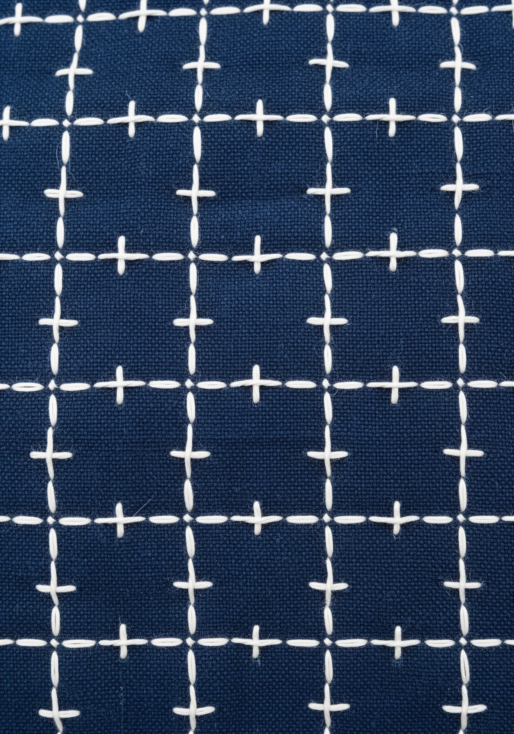 A modern Sashiko-inspired grid of white running stitches on a dark blue fabric.