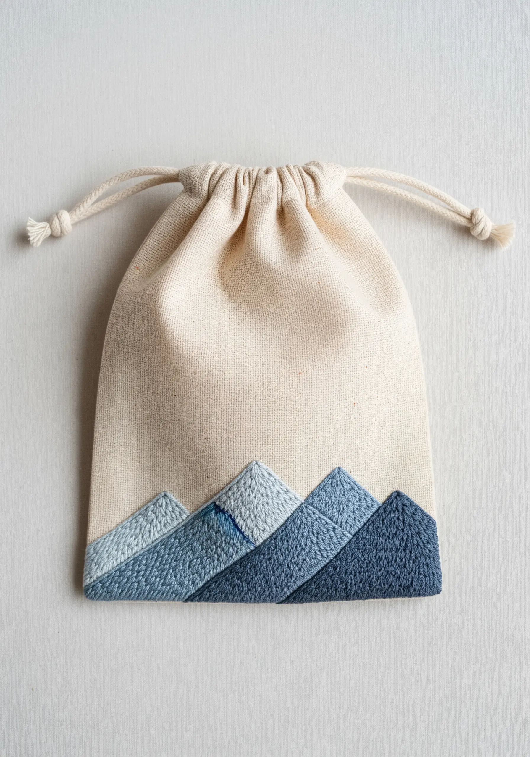 A drawstring pouch with an embroidered mountain range in shades of blue.