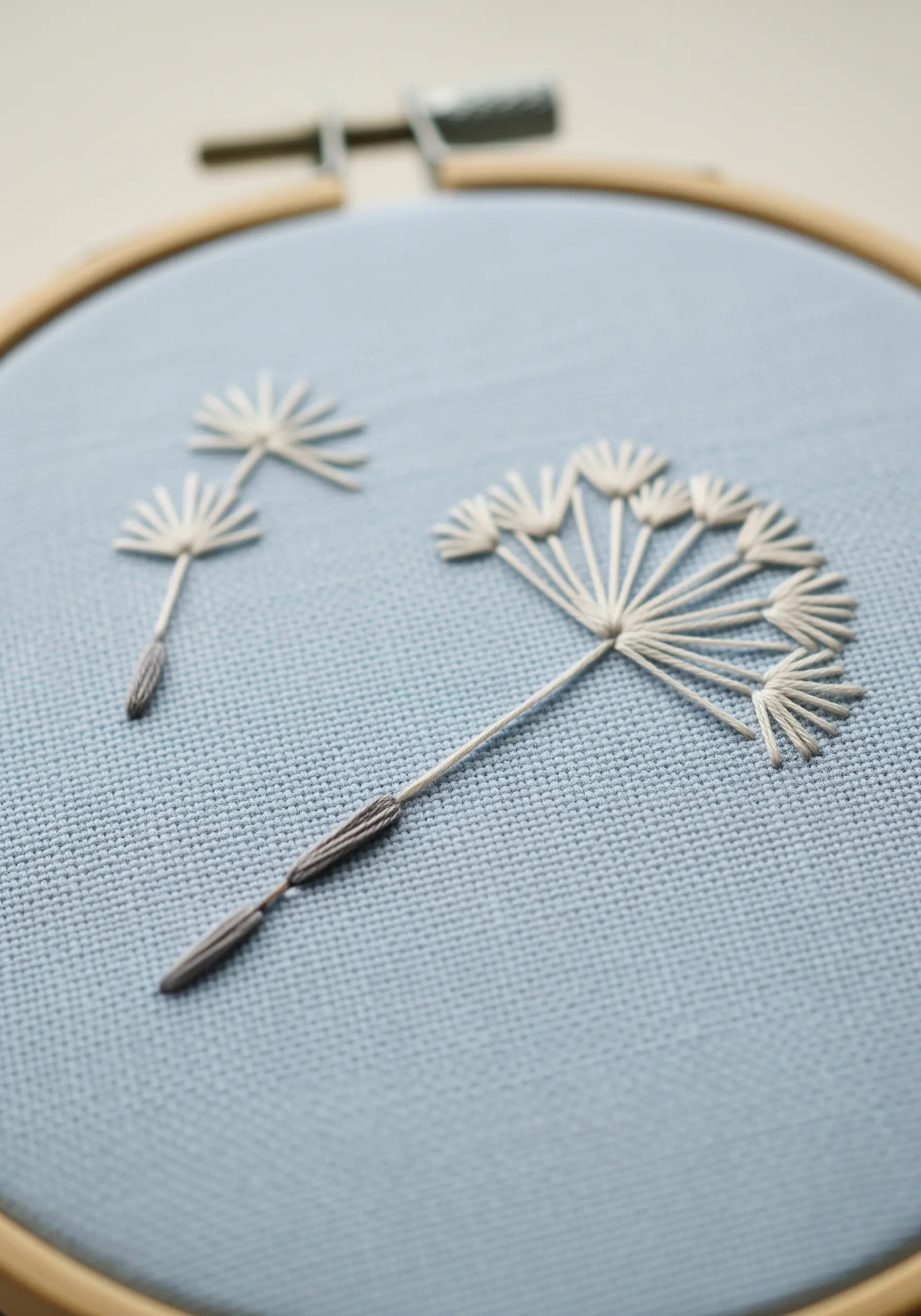 Delicate dandelion seed heads embroidered with white detached straight stitches on blue fabric.