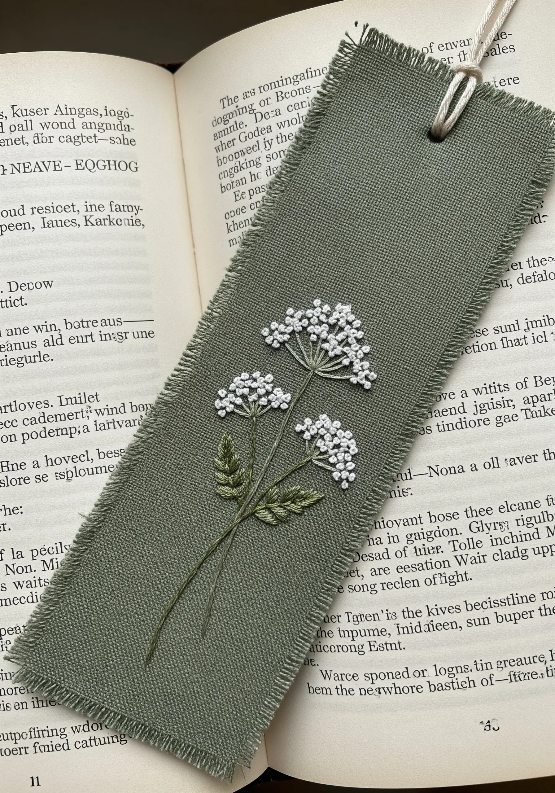 A sage green linen bookmark embroidered with delicate Queen Anne's Lace flowers.