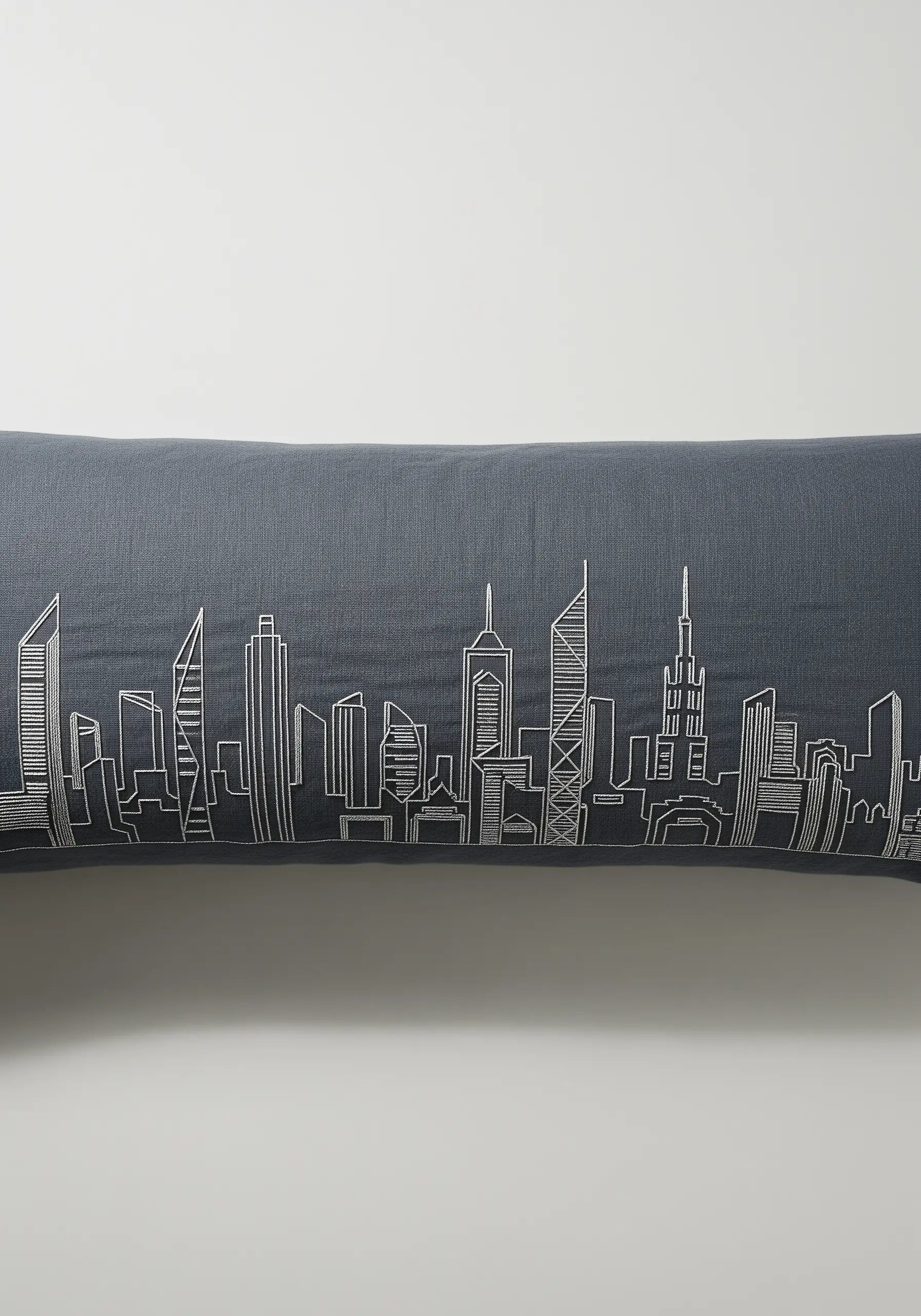 Intricate white line art of a city skyline stitched on a dark grey lumbar pillow.