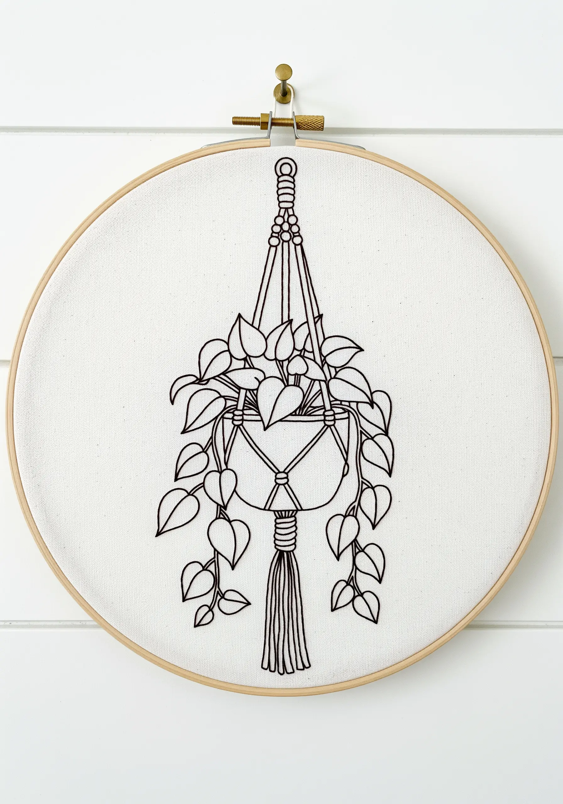 A minimalist line art embroidery of a Pothos plant in a macrame hanger.