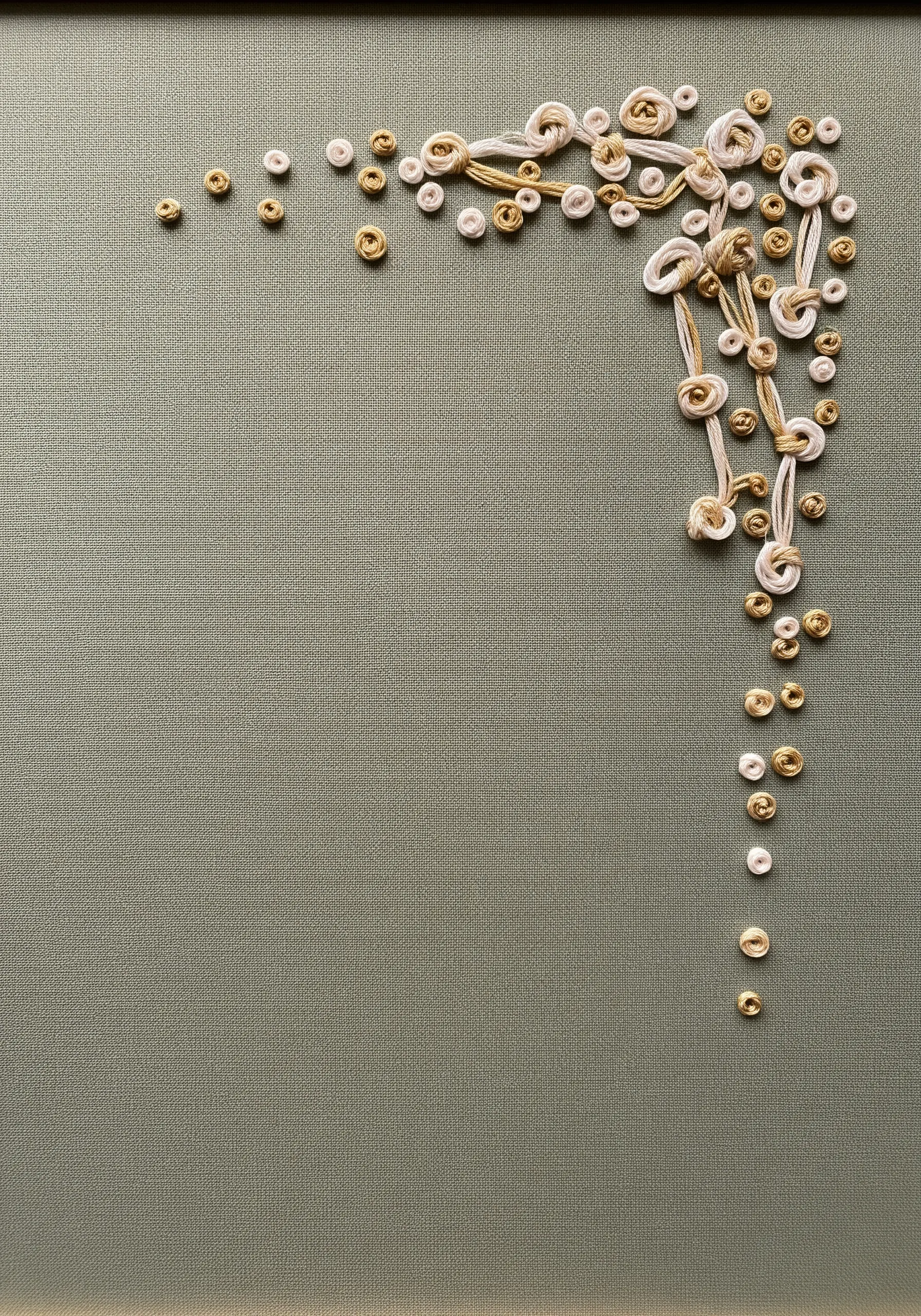 A cascade of cream and beige embroidery knots and loops in the corner of khaki fabric.