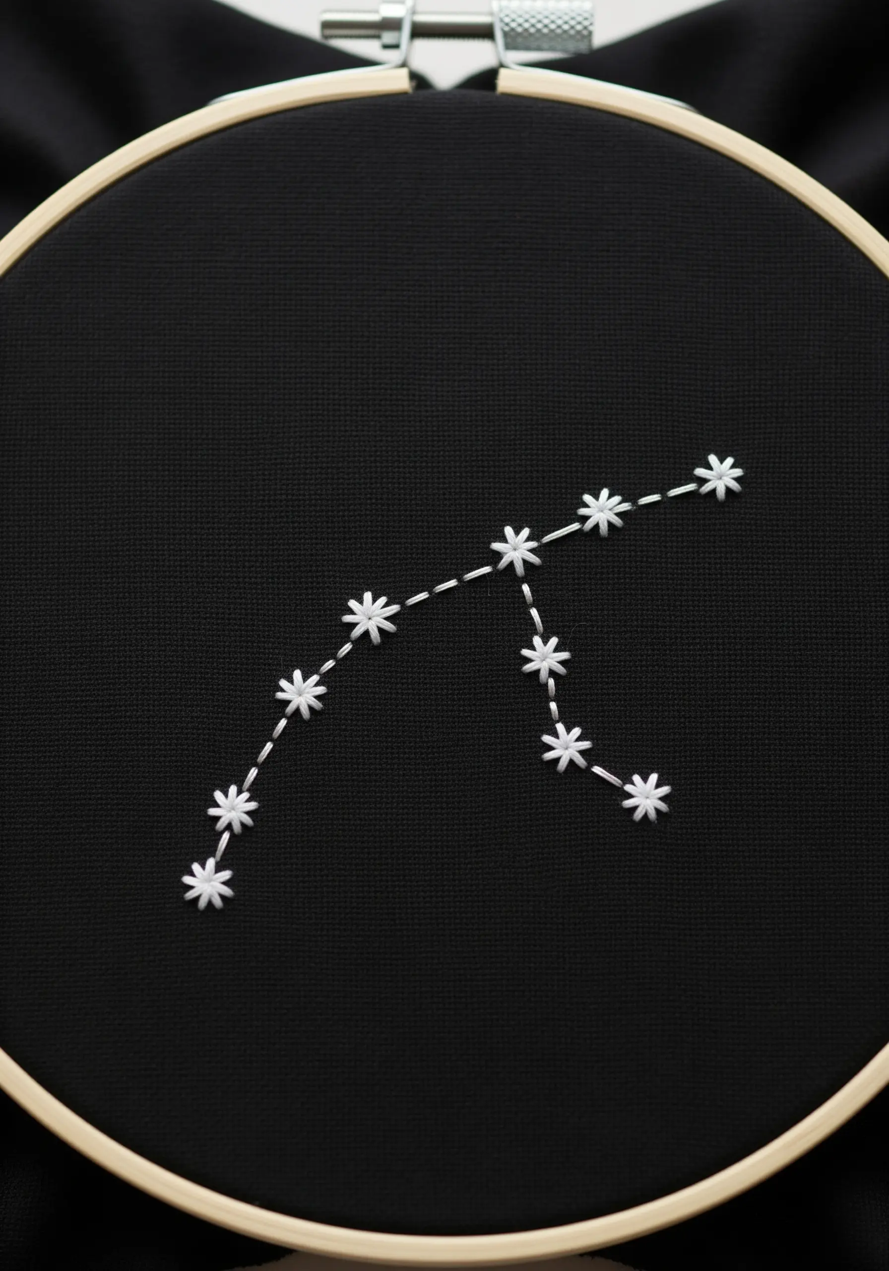 A white-thread constellation embroidered on black fabric in a wooden hoop.