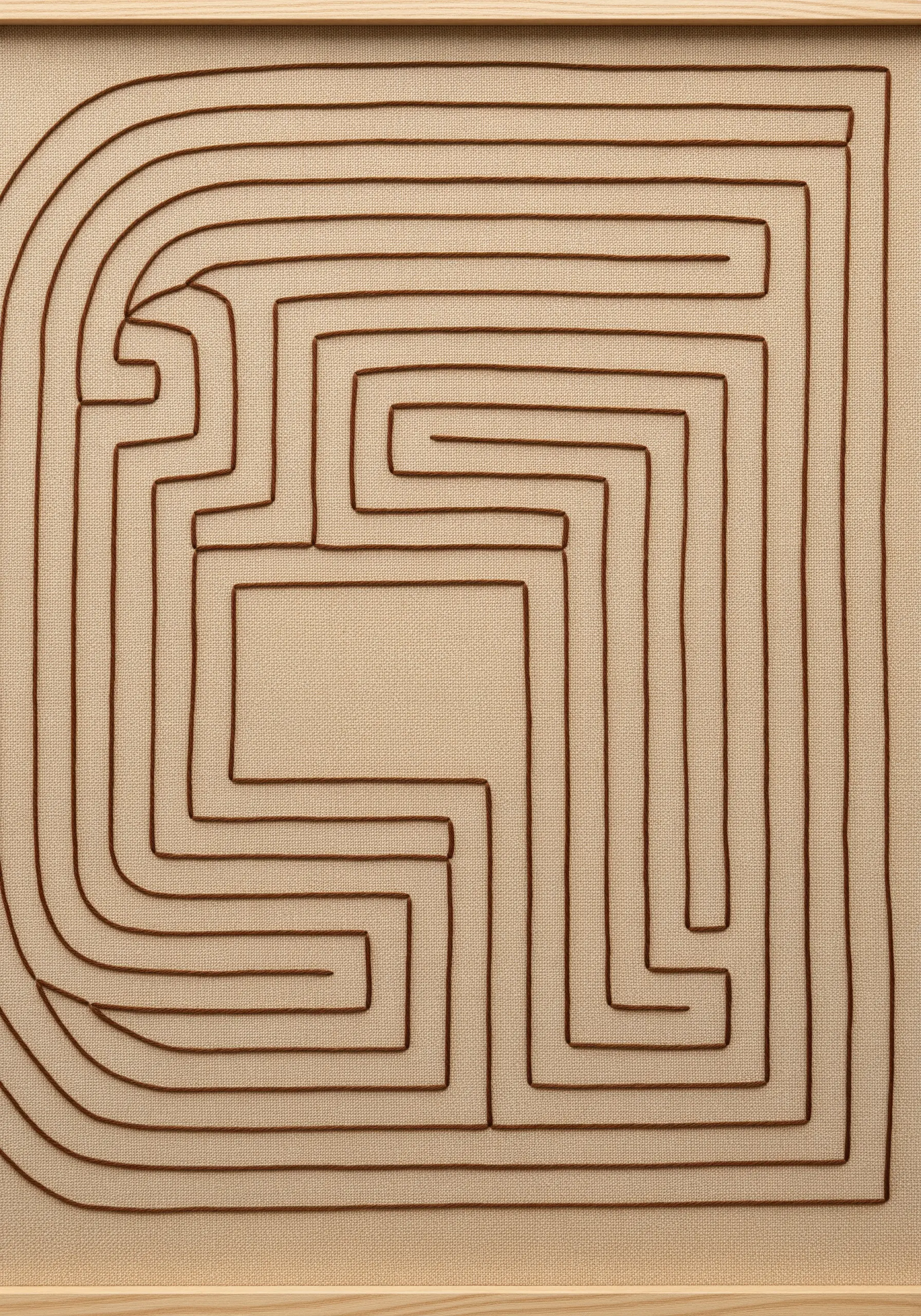 A close-up of a maze pattern created with a single brown cord couched onto neutral fabric.