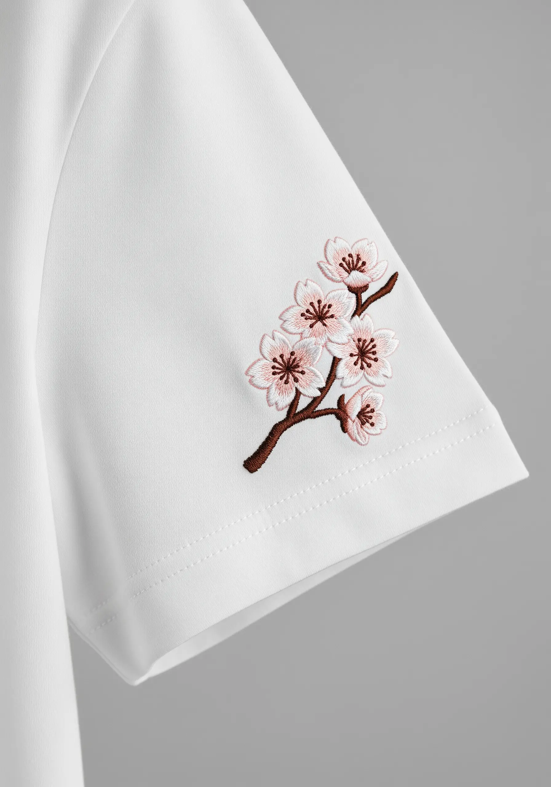 A branch of pink cherry blossoms embroidered on the crisp white sleeve of a T-shirt.
