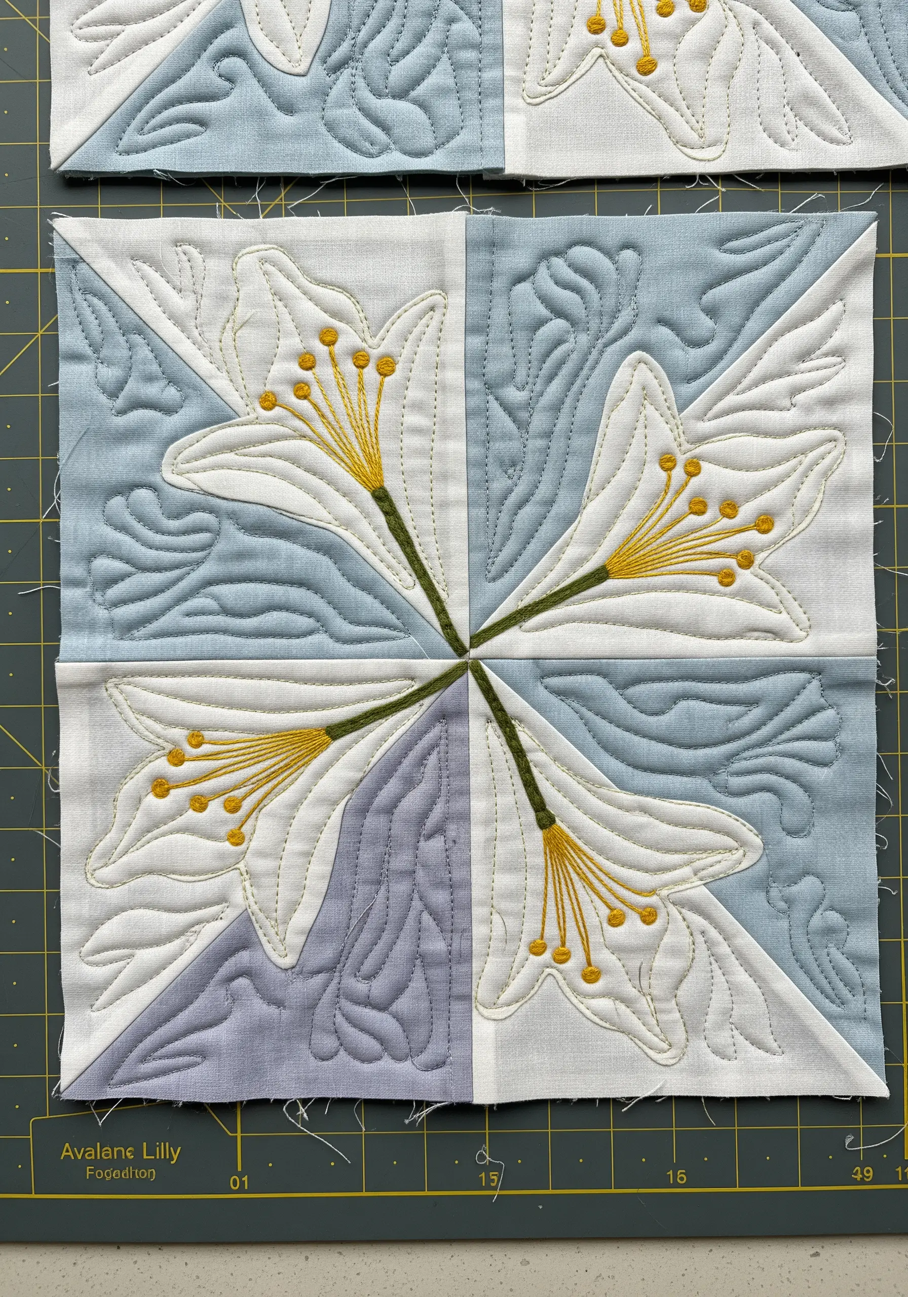 A quilted block with four white lily motifs defined by embroidery and background quilting